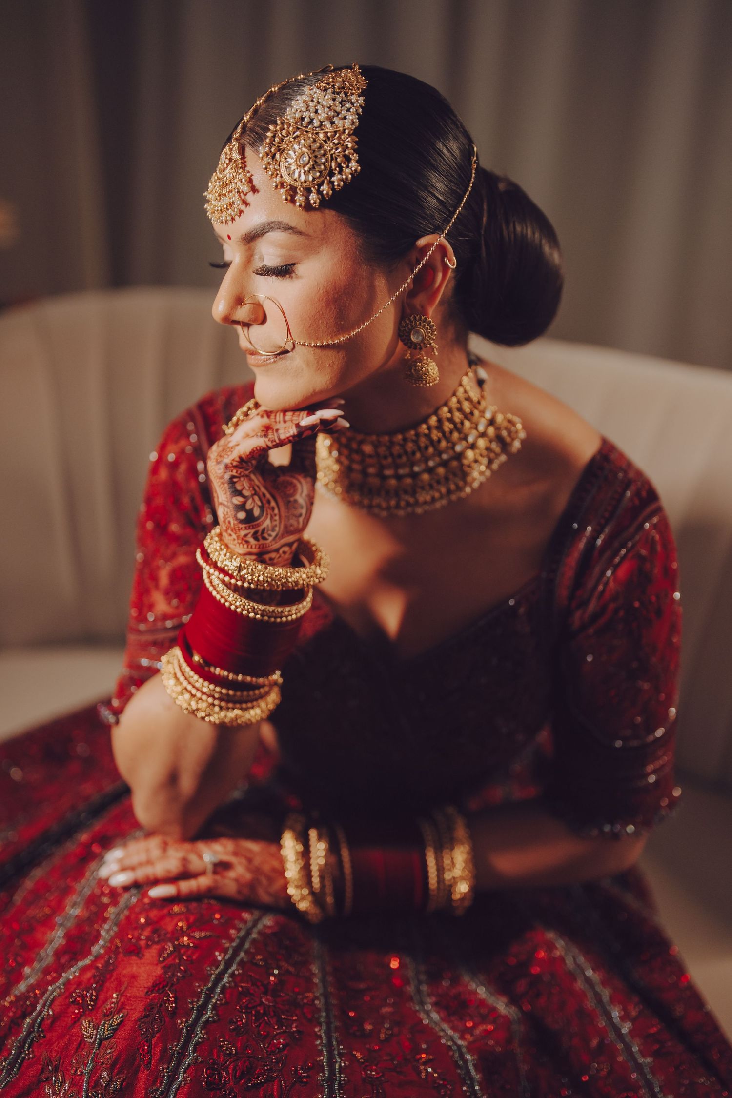 Elegant bridal portrait showcasing traditional red lehenga and complete gold jewelry set in warm lighting.