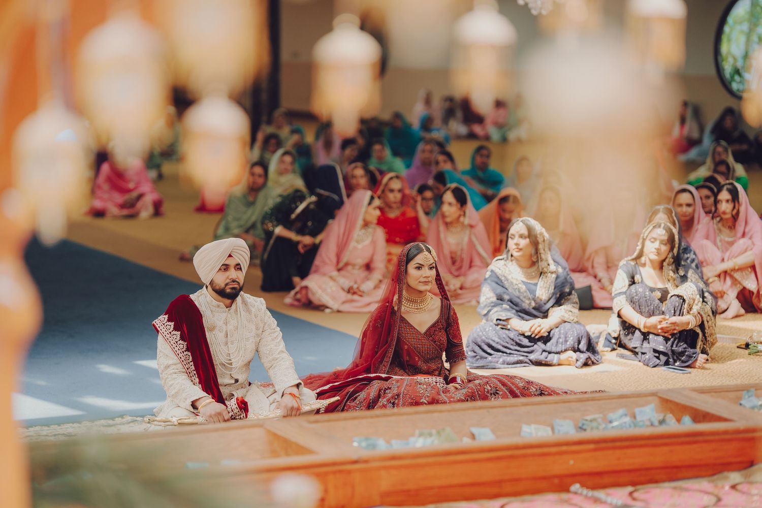 Sikh wedding ceremony with guests seated on floor during traditional rituals.