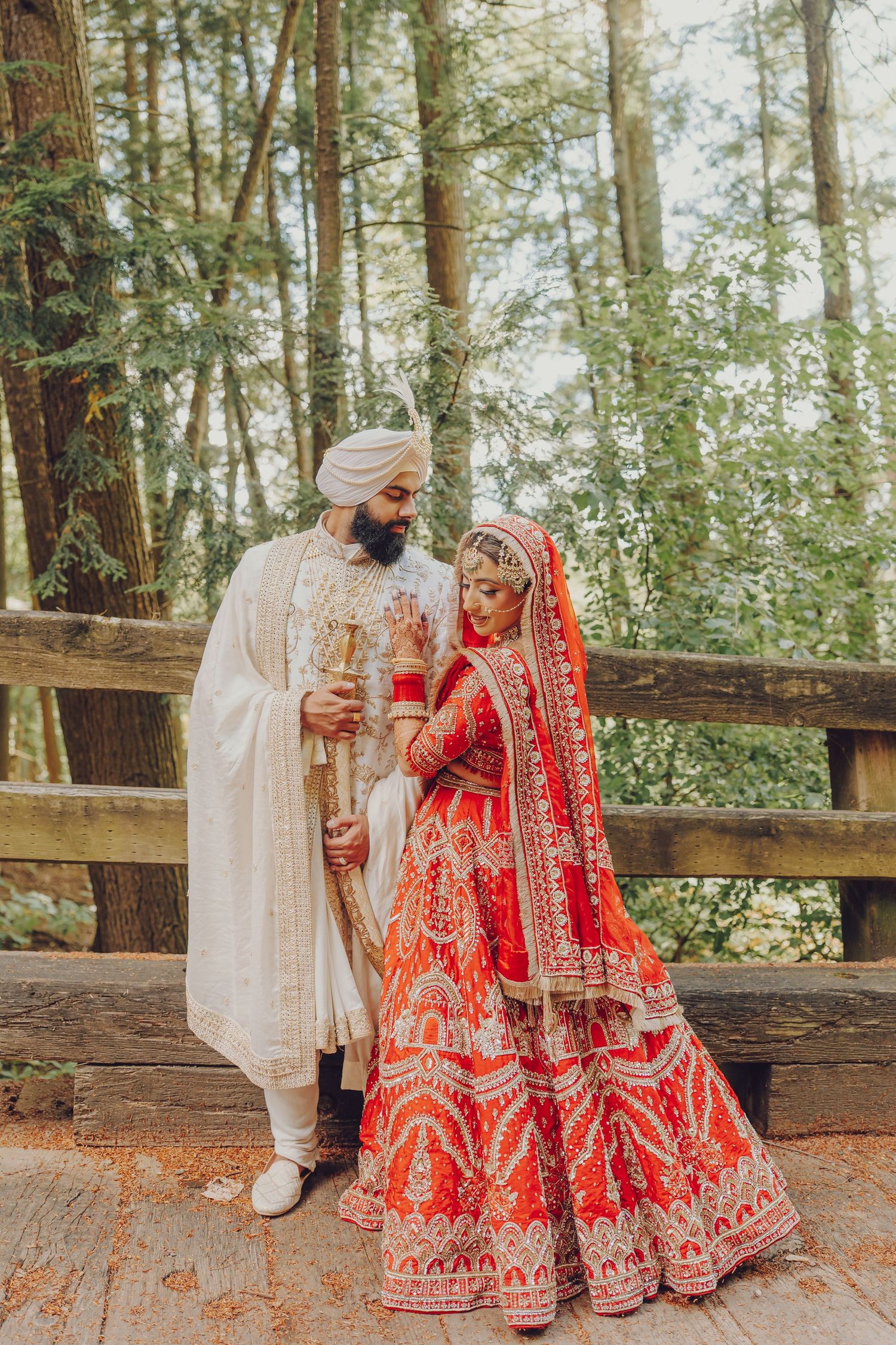 Couple in traditional Indian wedding attire sharing a moment on rustic wooden deck in forest setting.