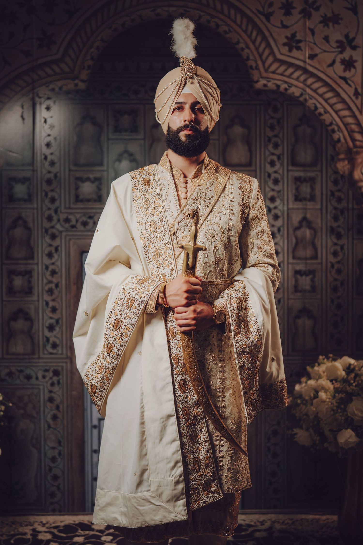 Groom in traditional cream and gold Sikh wedding attire holding ceremonial sword.
