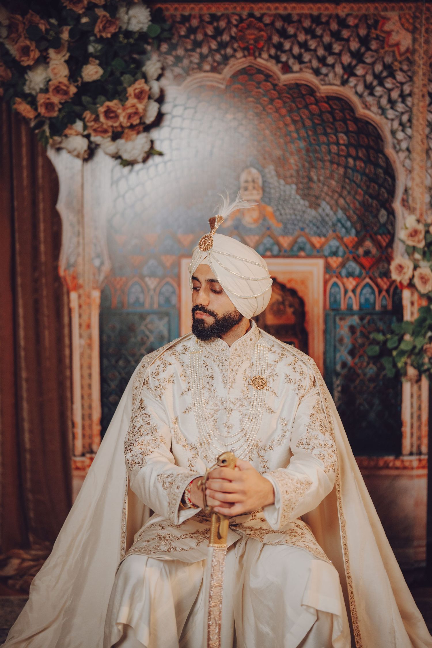 Traditional Sikh groom wearing an ornate white sherwani and turban in an elegant setting.