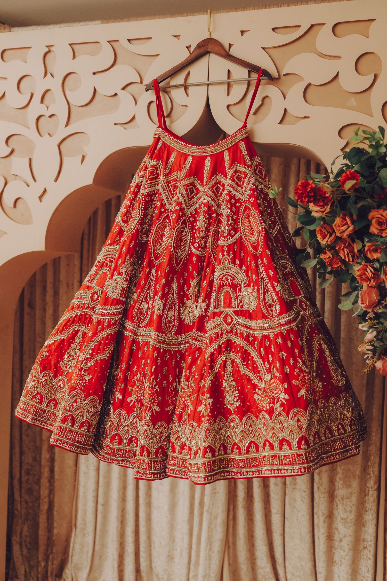 Ornate red and gold traditional Indian lehenga dresses hanging on display against a decorative wall.