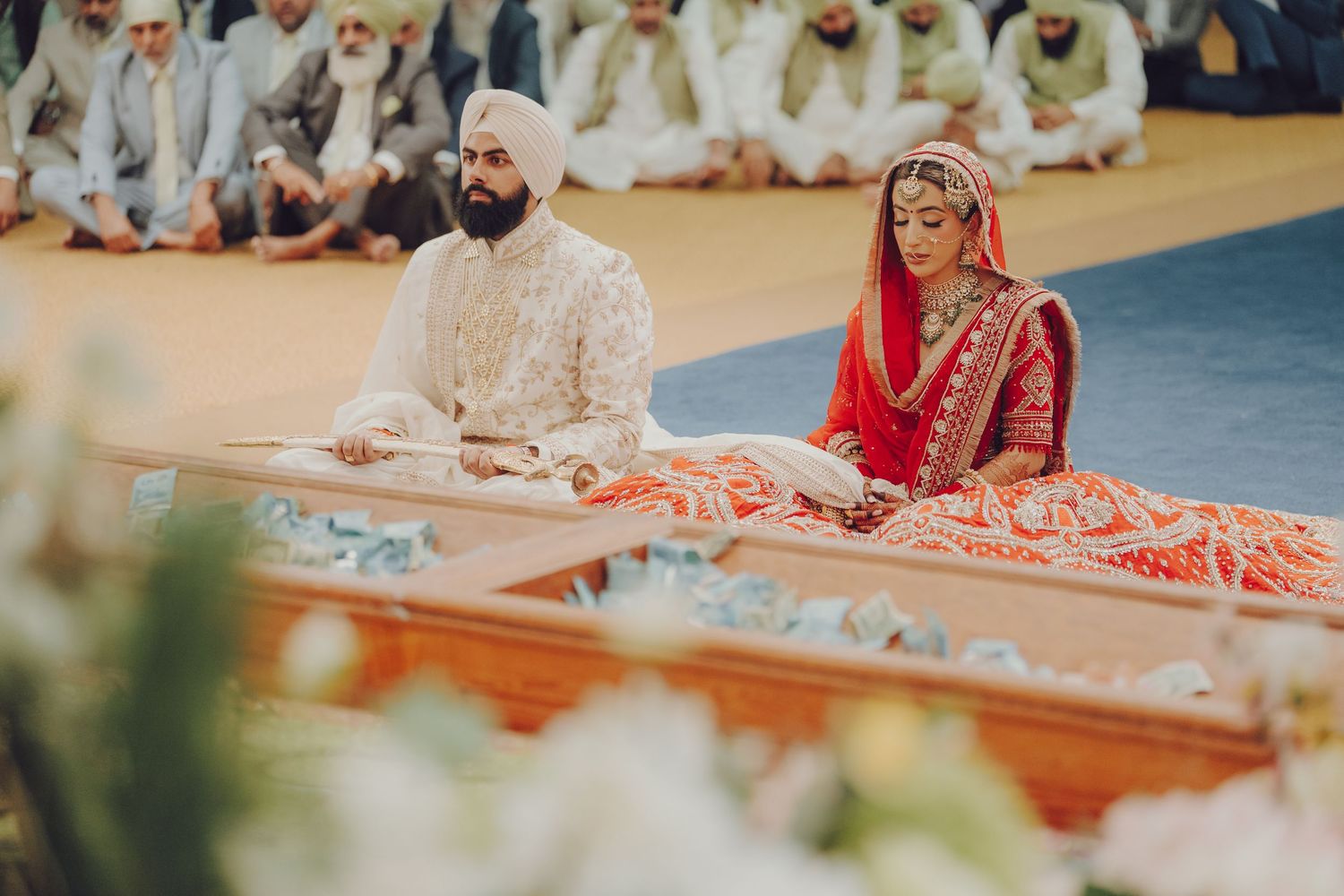 A panoramic view of a traditional Sikh wedding ceremony taking place in a Gurdwara with guests seated on the floor.