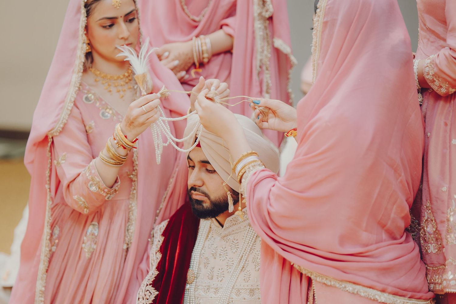 Traditional Sikh wedding ceremony with attendants in flowing pink dresses helping adjust ceremonial attire.