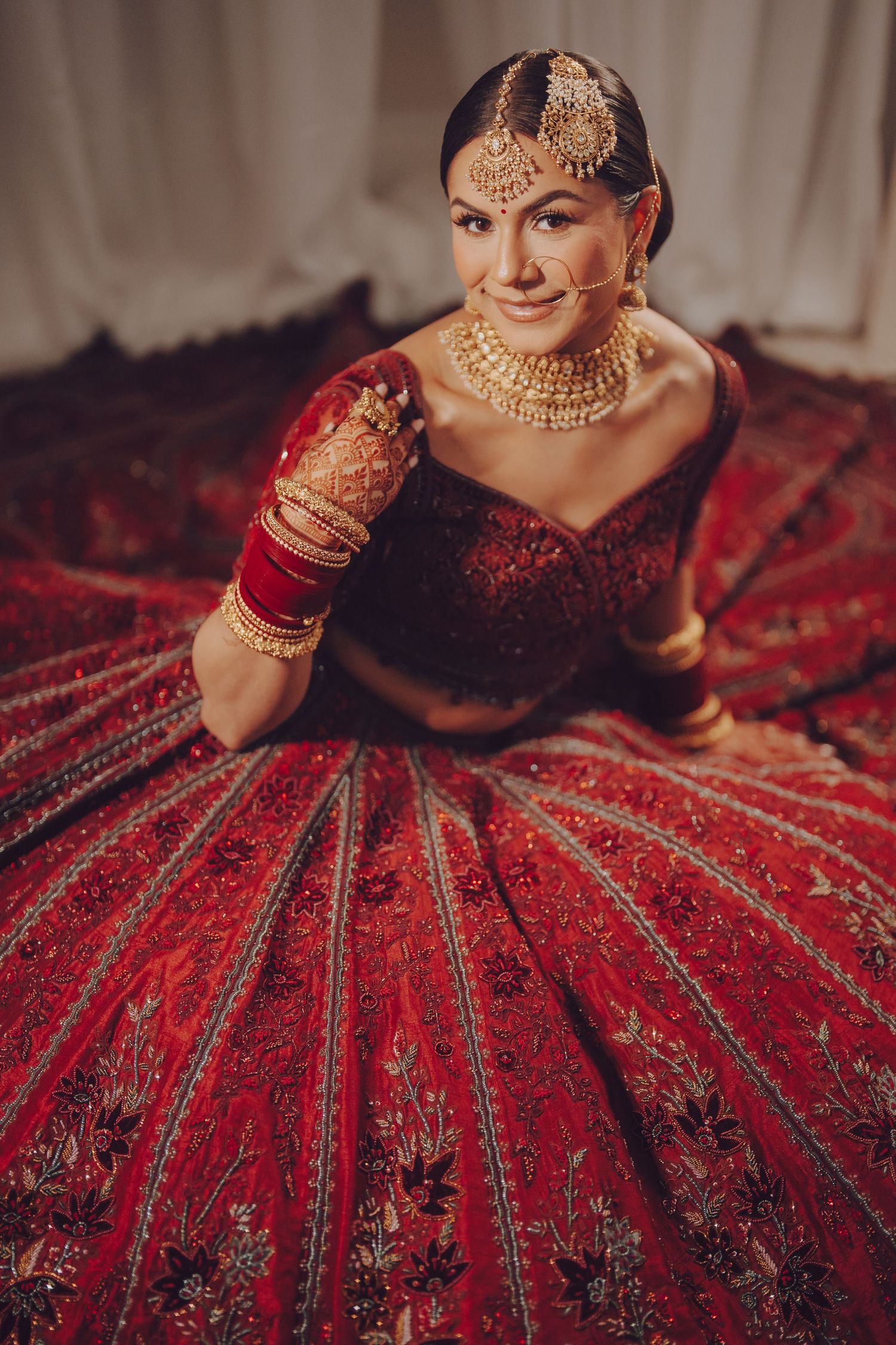 Traditional Indian bride in an ornate red and gold lehenga with intricate embroidery and jewelry details.