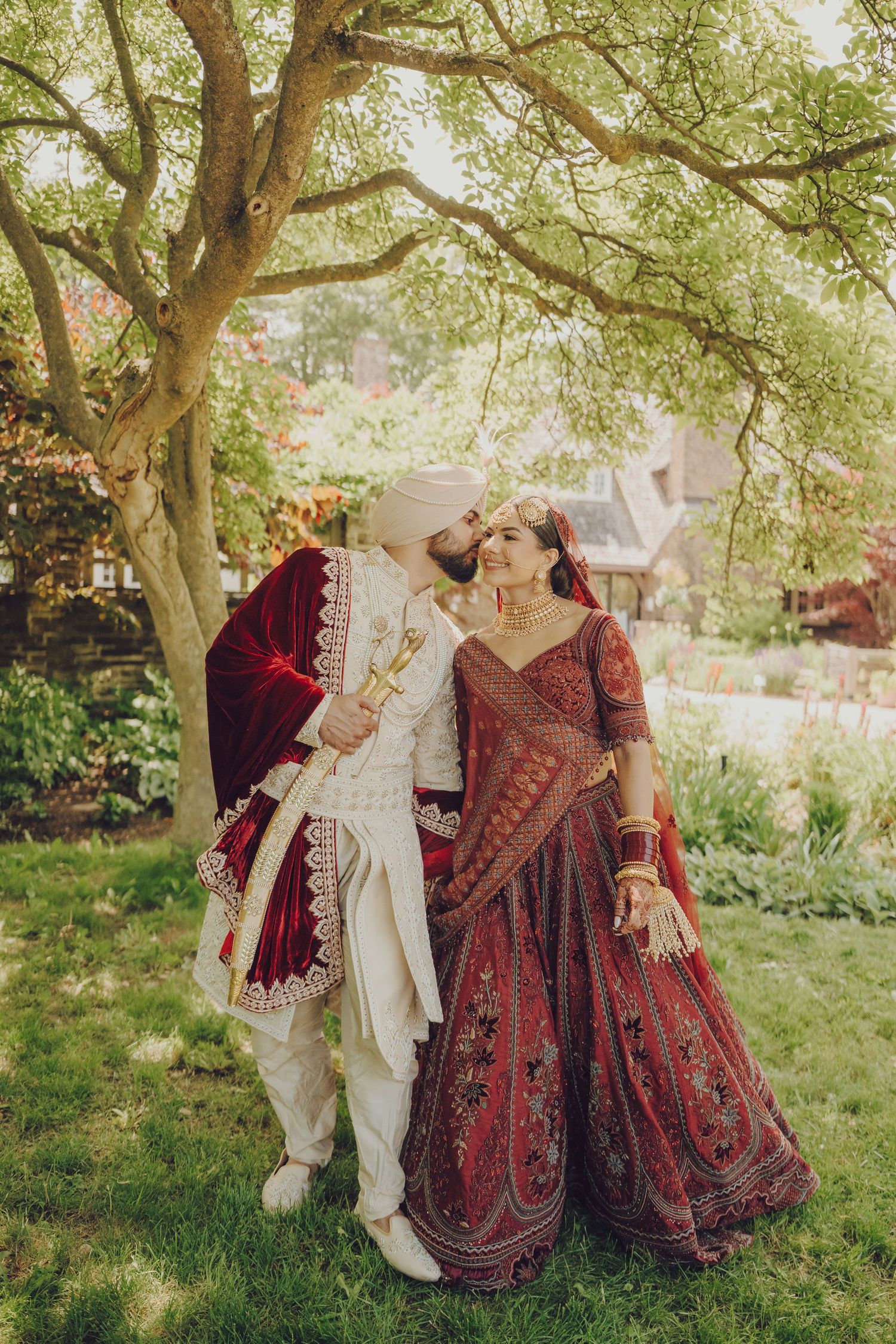A couple in vintage-inspired attire dances together under green trees in a romantic outdoor setting.