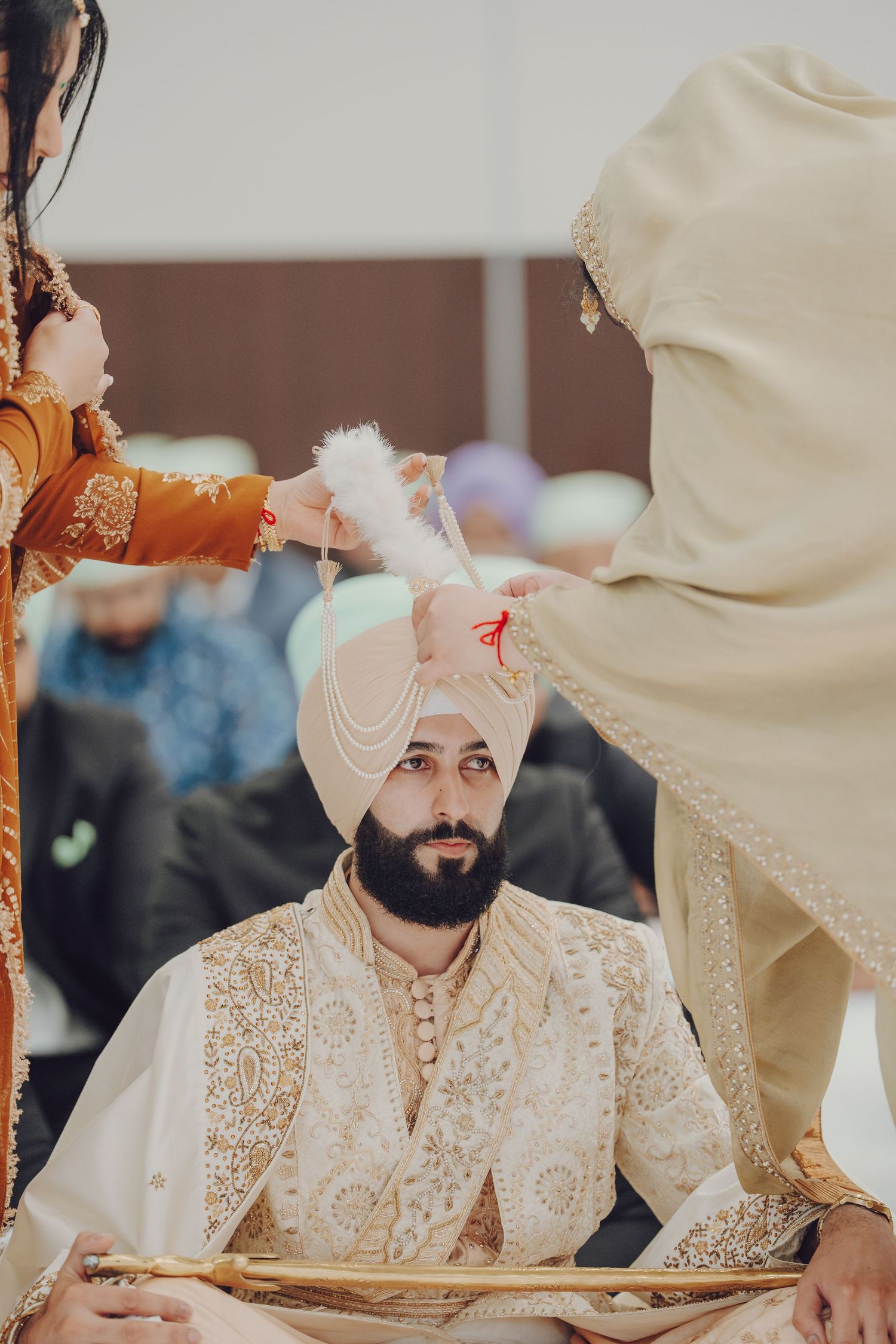 Sikh wedding ceremony participants seated in traditional cream and gold embroidered attire during religious proceedings.