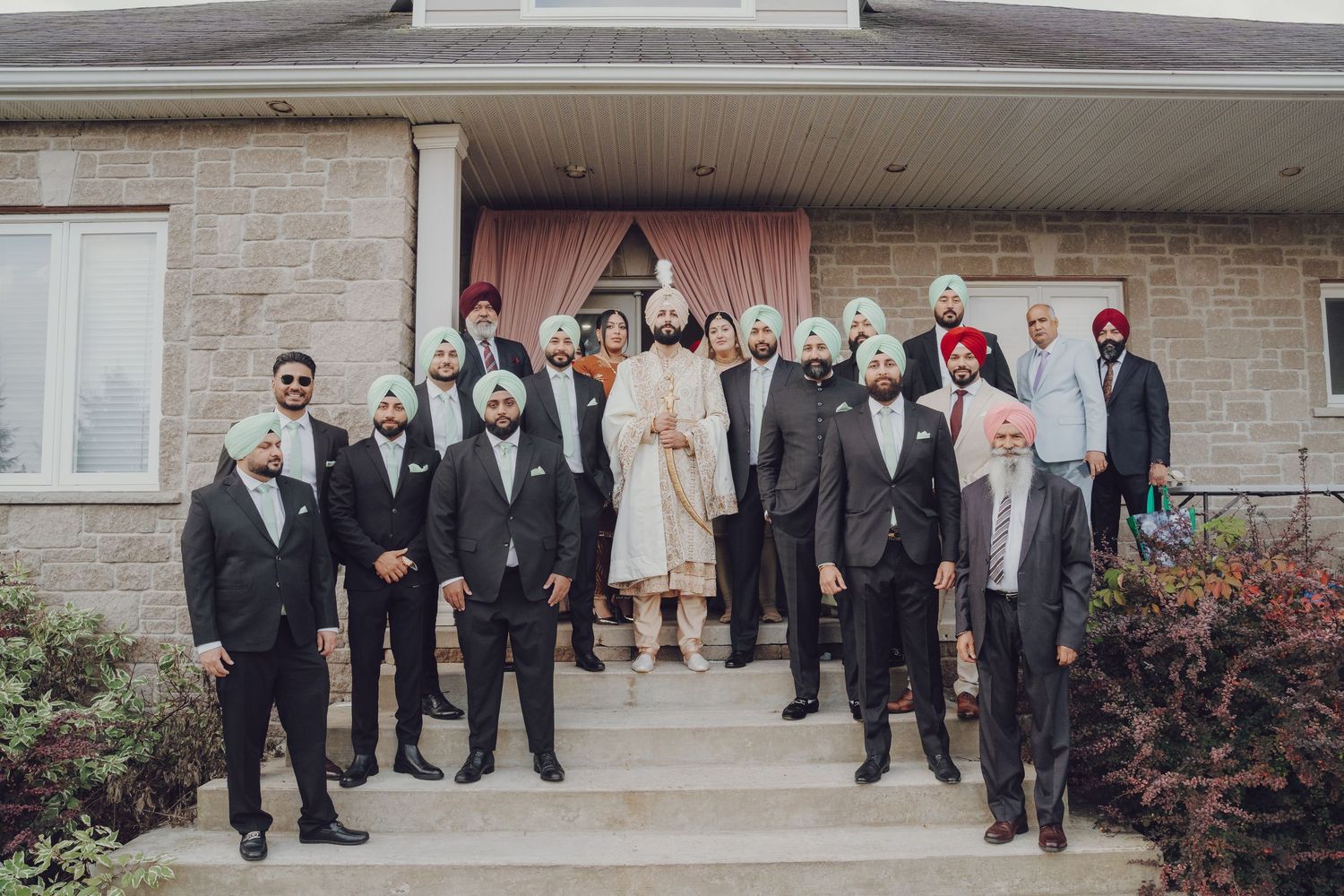 Group of formally dressed people in suits standing on steps outside a stone building.