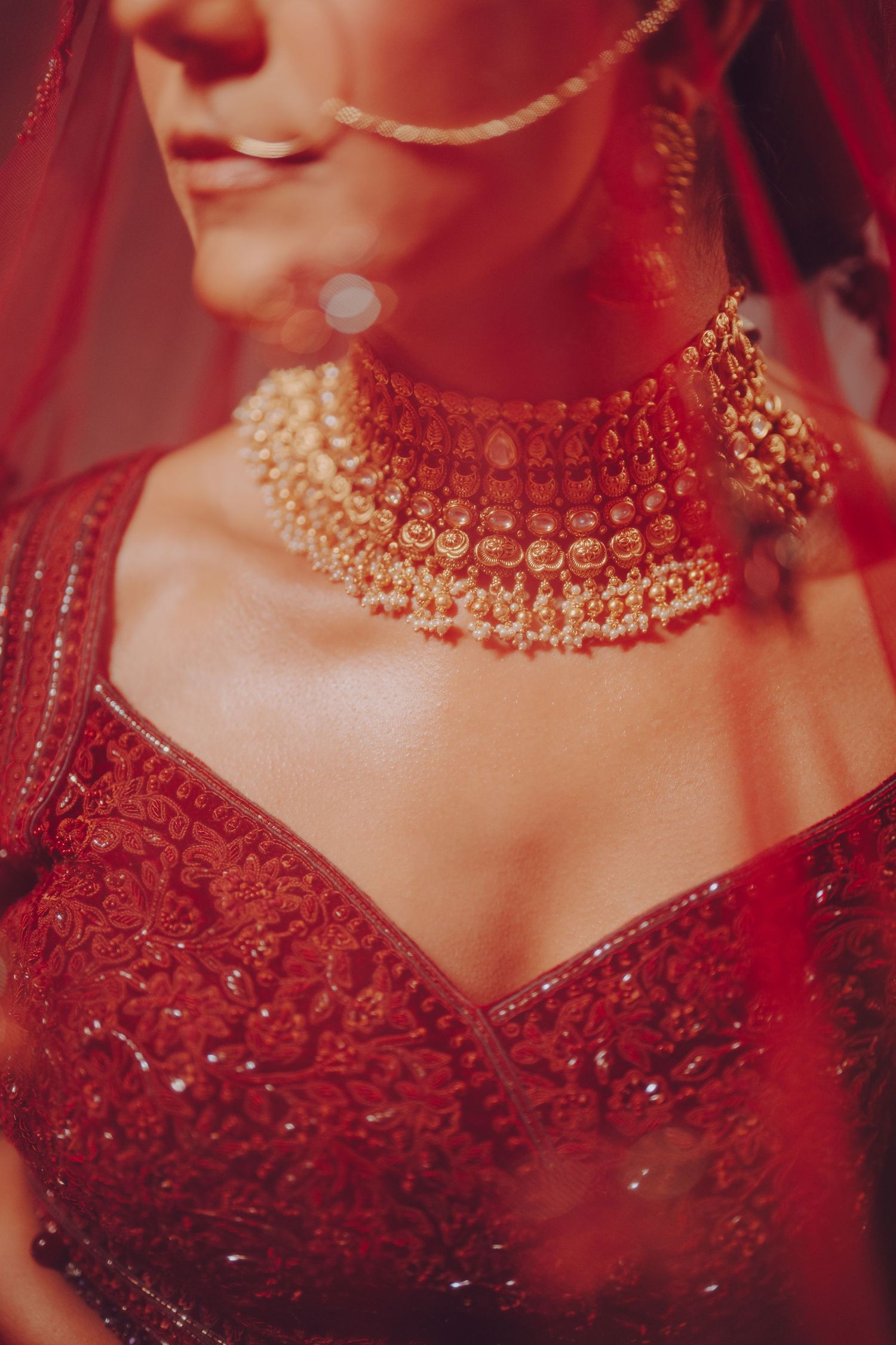 Close-up details of ornate gold jewelry and red embroidered fabric from traditional Indian bridal attire.