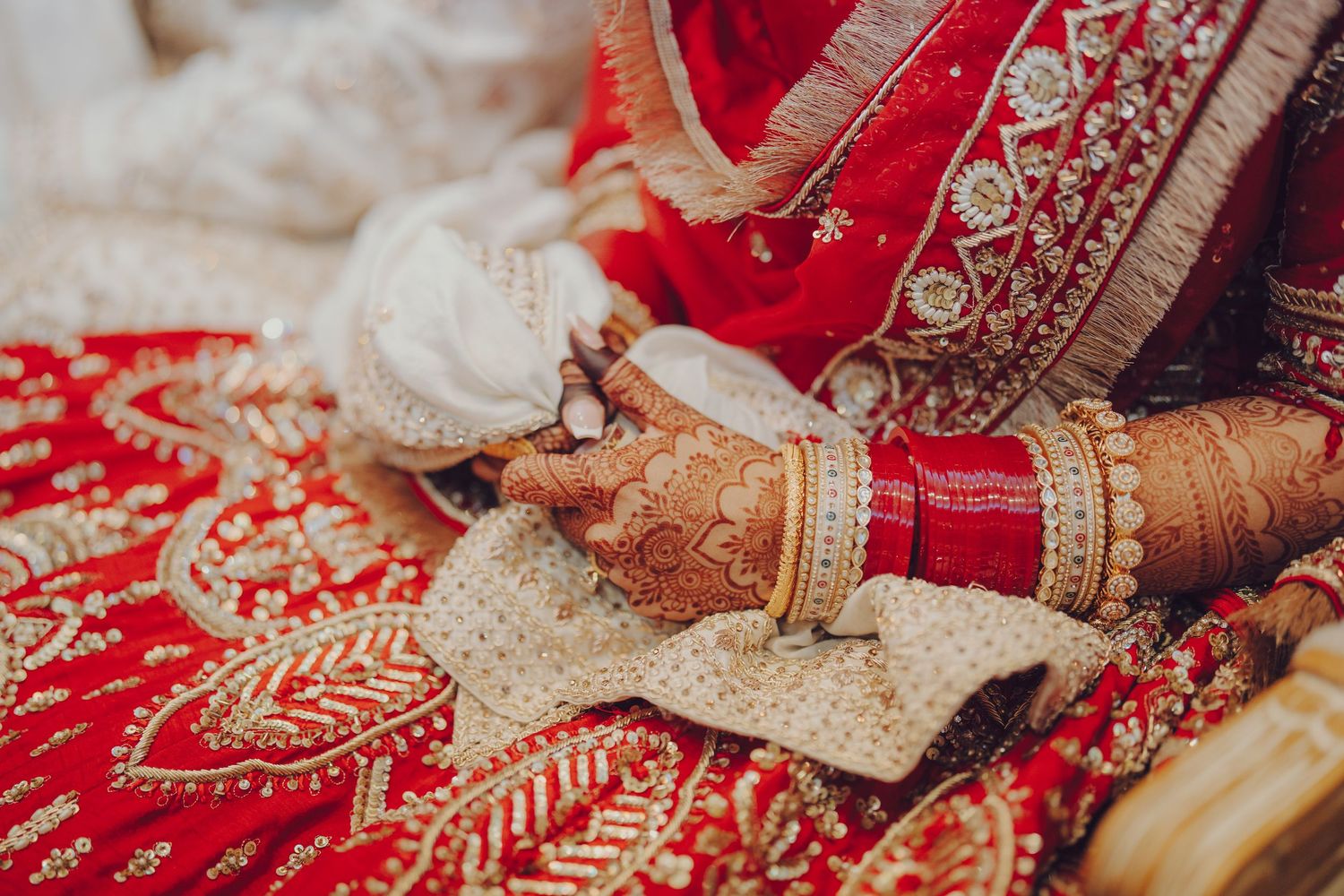 Ornate gold and red Indian bridal jewelry and accessories displayed on embroidered fabric with traditional designs.