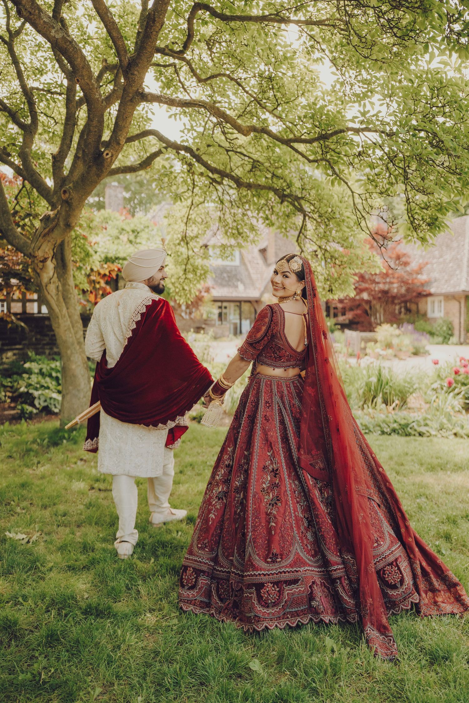 Ornate red and gold Indian wedding lehenga displayed in a lush garden setting.