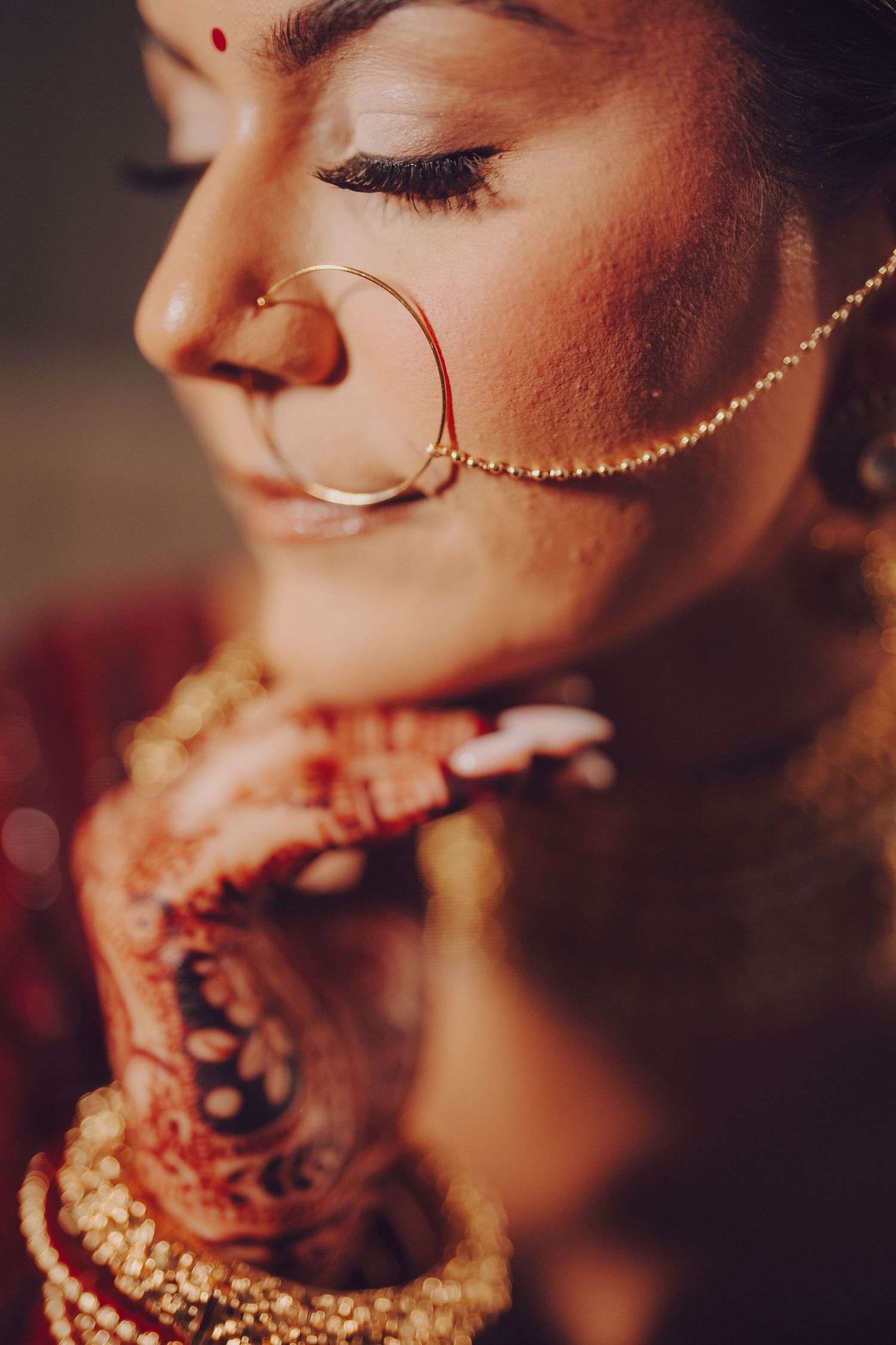 Artistic close-up of traditional Indian bridal nose ring and mehndi details in warm tones.