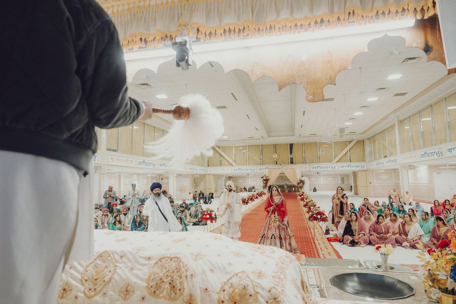 Photographer capturing a traditional Sikh wedding ceremony in a decorated hall.