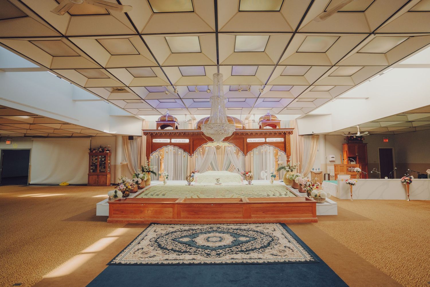 Interior panorama of a large empty prayer hall with ornate ceiling design and carpeted floor.