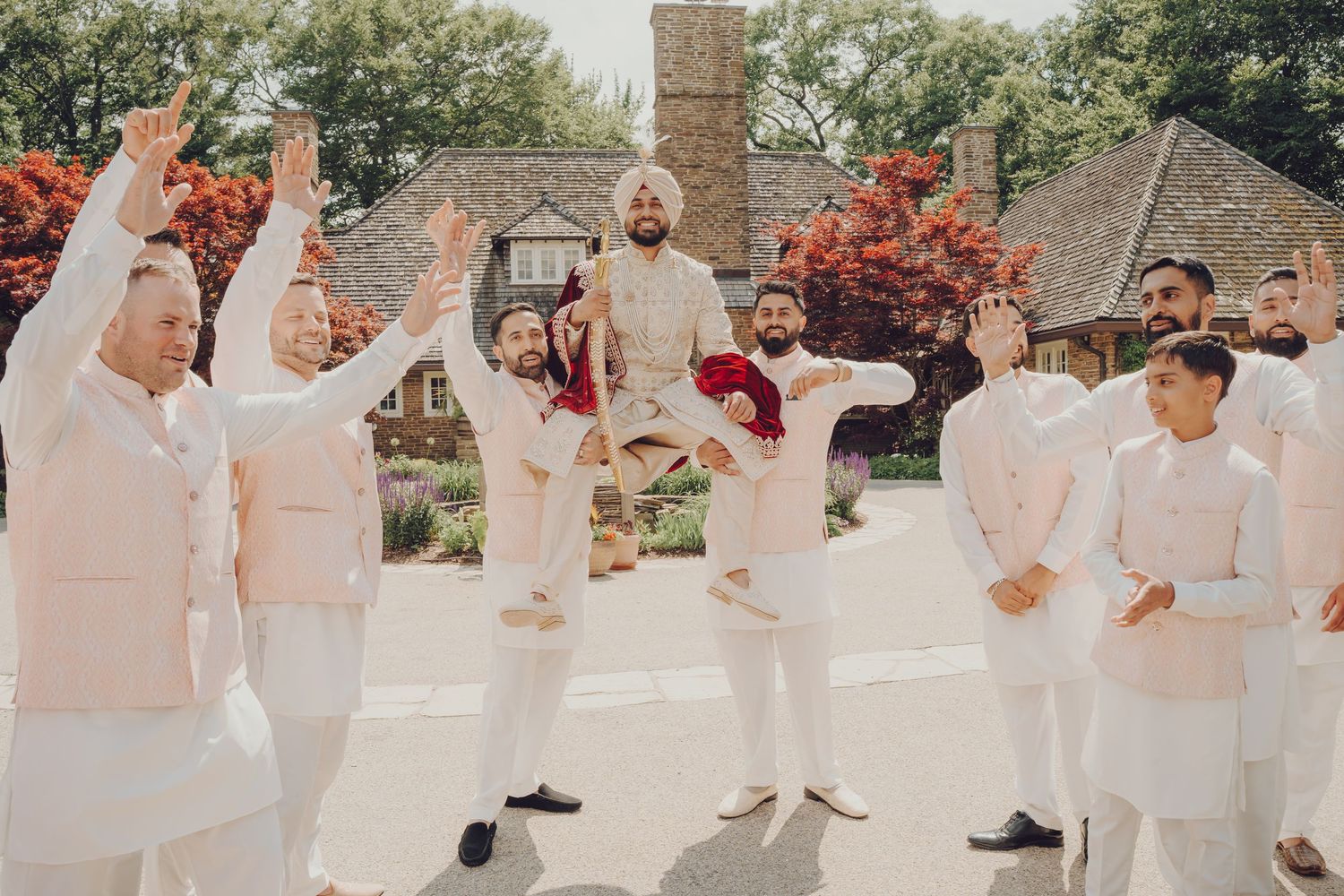 Group celebration shot with people in traditional white Indian attire against brick architecture.