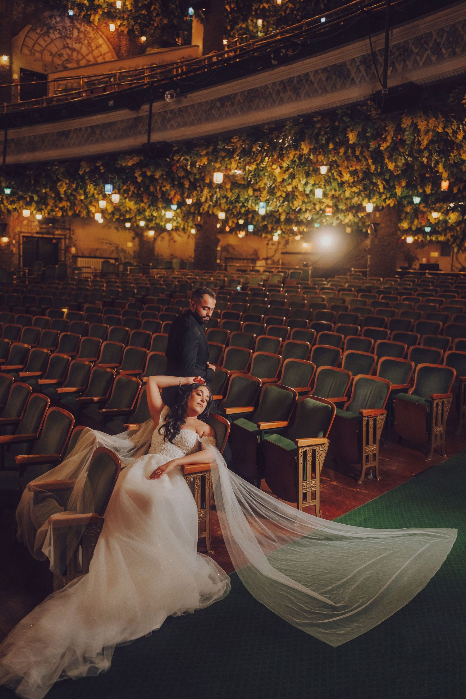 Dramatic bridal photoshoot in an empty theater with flowing white dress and veil against rows of vintage seats.