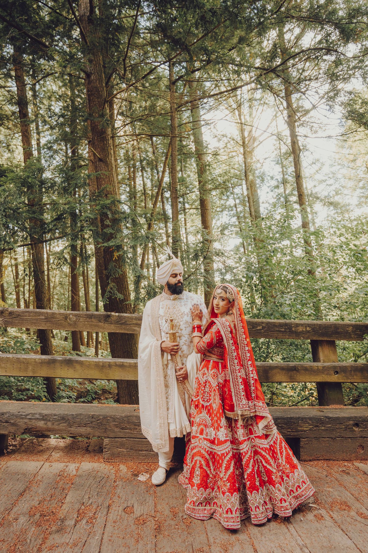 Sikh wedding couple on wooden deck surrounded by forest scenery.