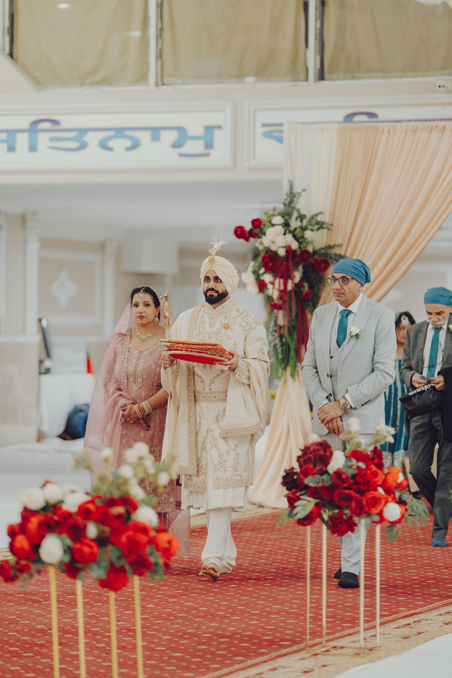 Sikh wedding ceremony in progress with red floral decorations in a temple setting.