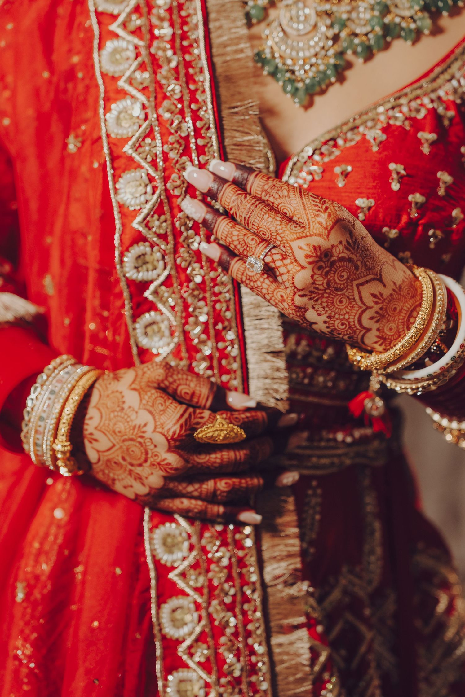 Intricate henna designs adorned hands wearing traditional Indian wedding bangles against a red bridal lehenga background.