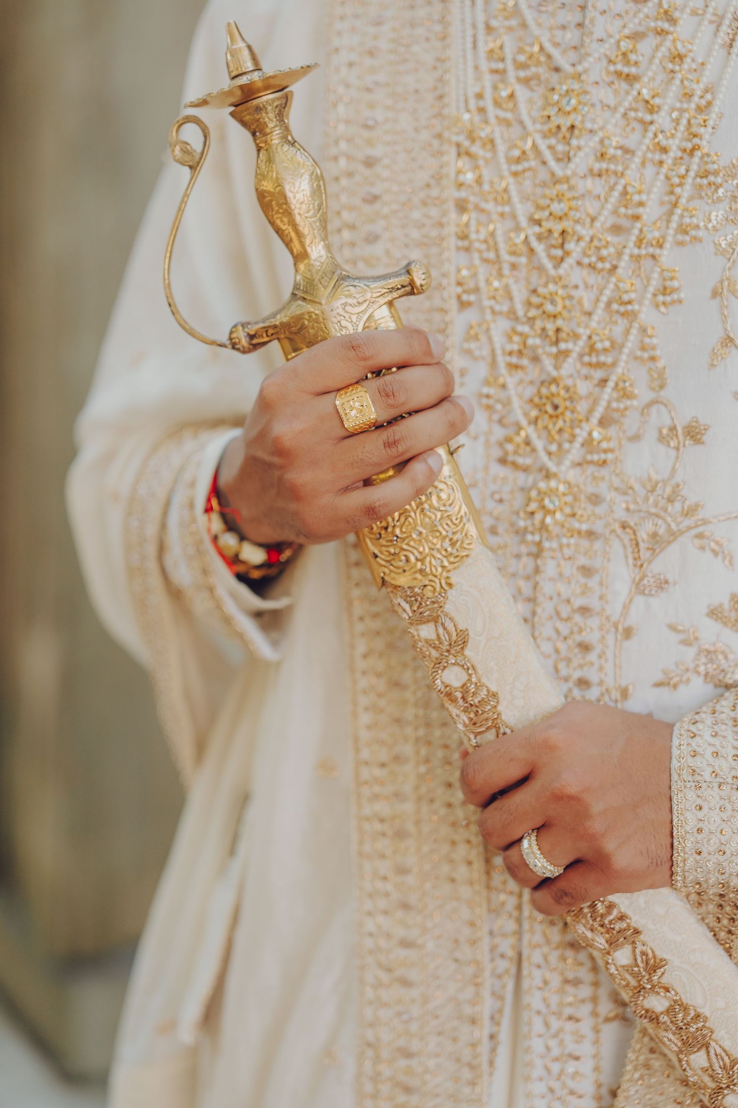 Close-up of ornate gold kirpan ceremonial dagger with detailed embellishments against traditional white wedding attire.
