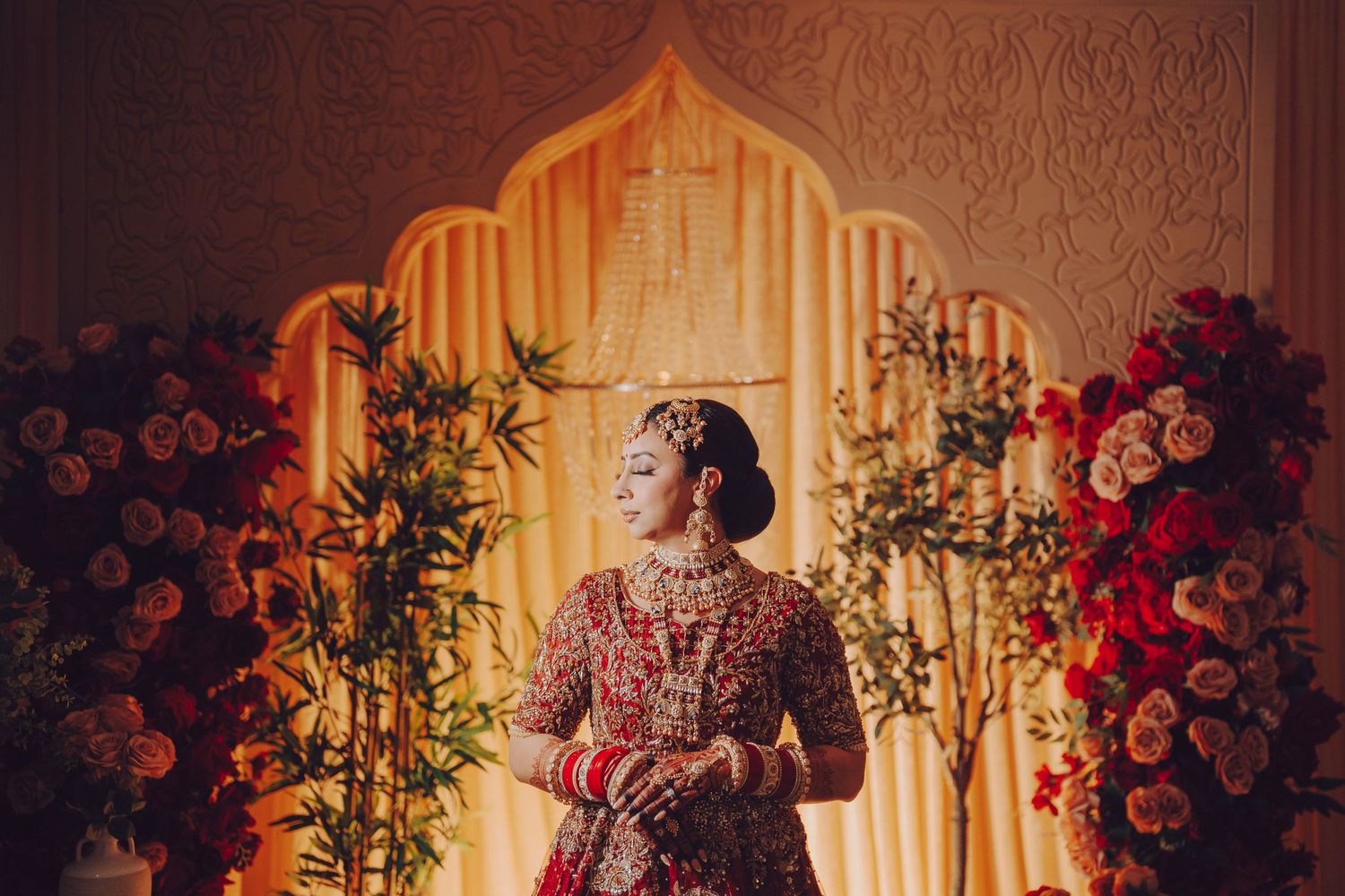 A romantic candlelit wedding reception venue decorated with red roses and greenery creates a warm ambiance.