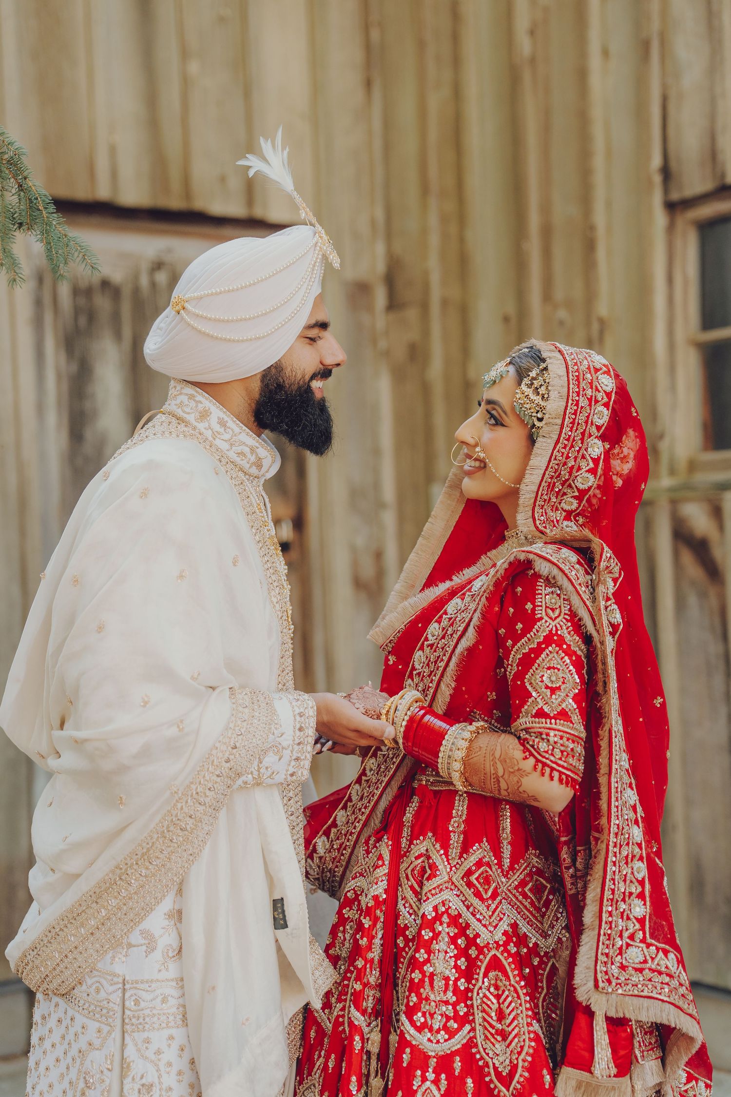 Wedding couple in traditional Sikh attire sharing a moment against wooden wall backdrop.