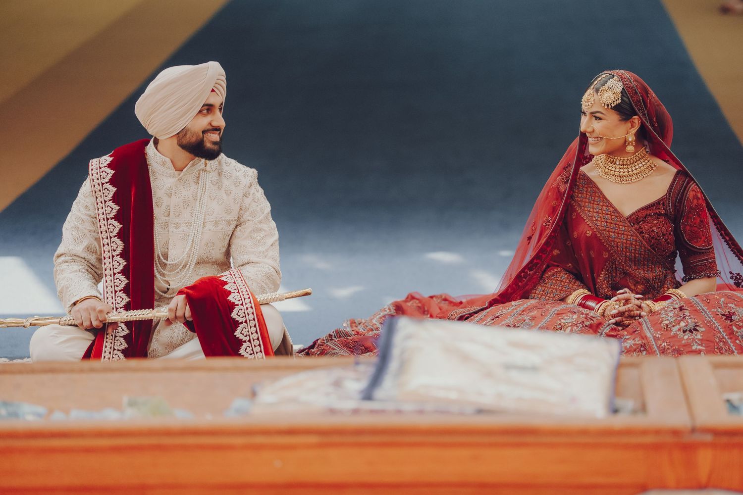 Traditional Sikh wedding ceremony with couple seated on floor in ceremonial attire.