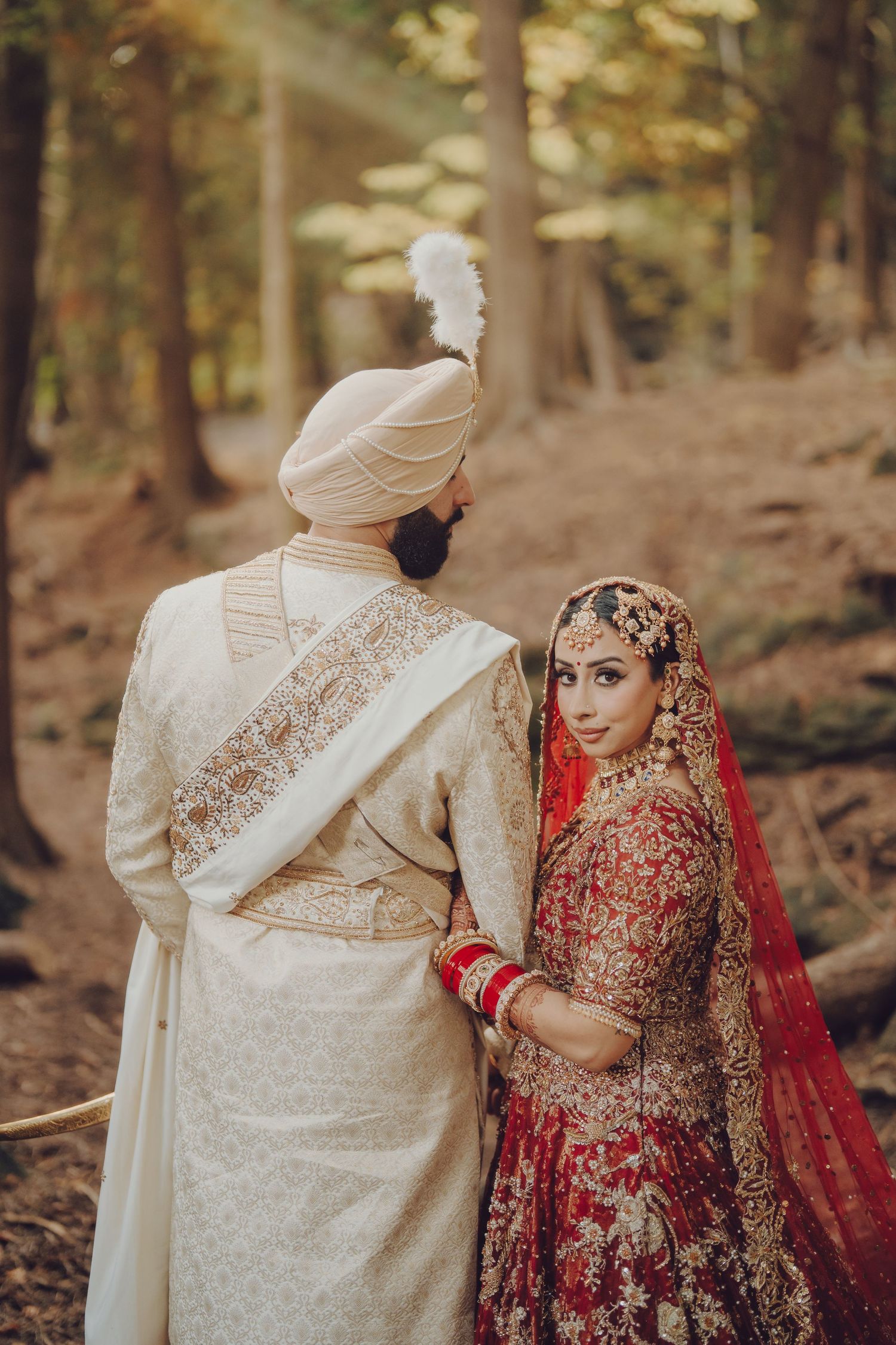 Couple in traditional South Asian wedding attire share intimate moments in a woodland setting.