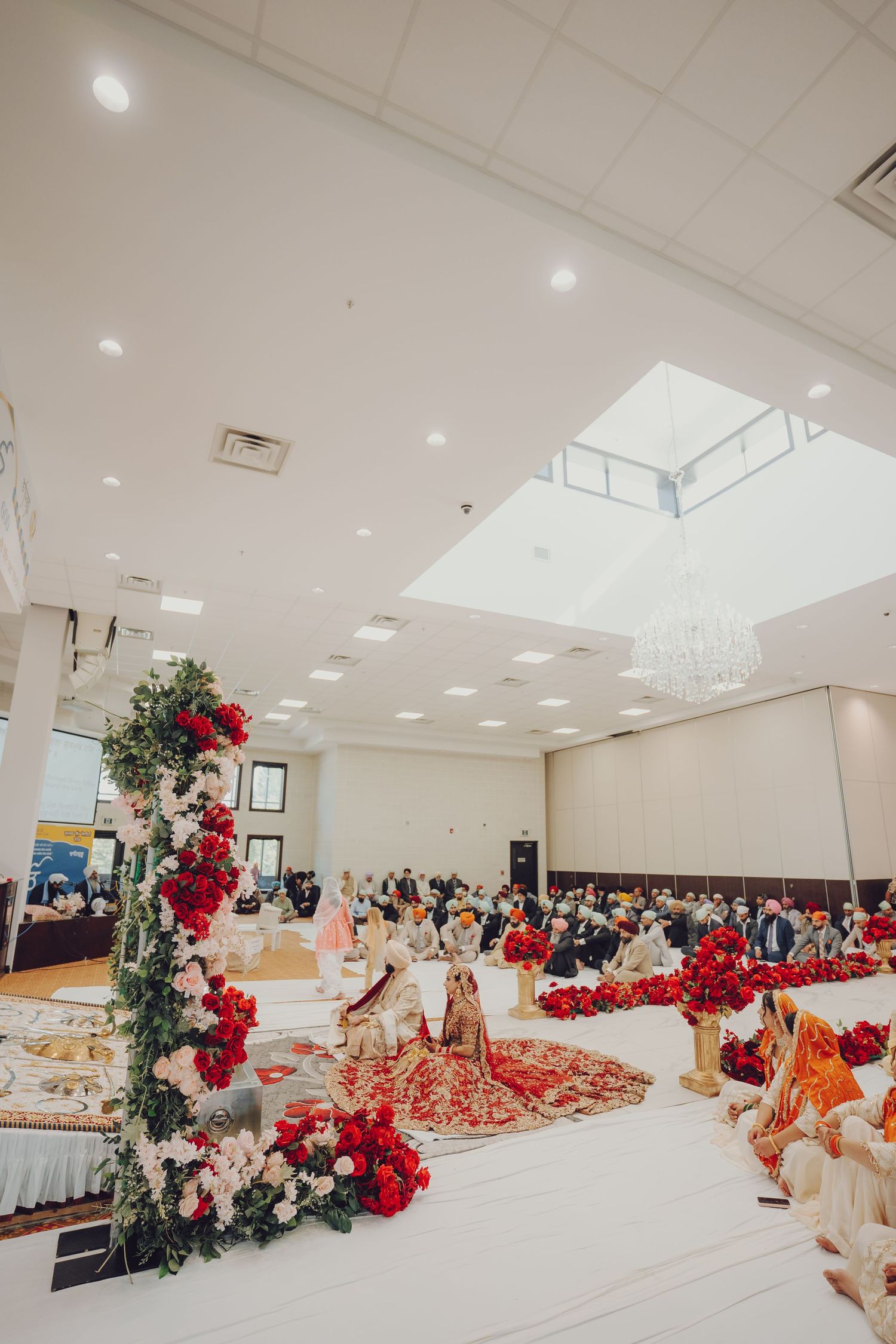 Wide view of an indoor wedding venue decorated with red roses and white drapery for a South Asian ceremony.
