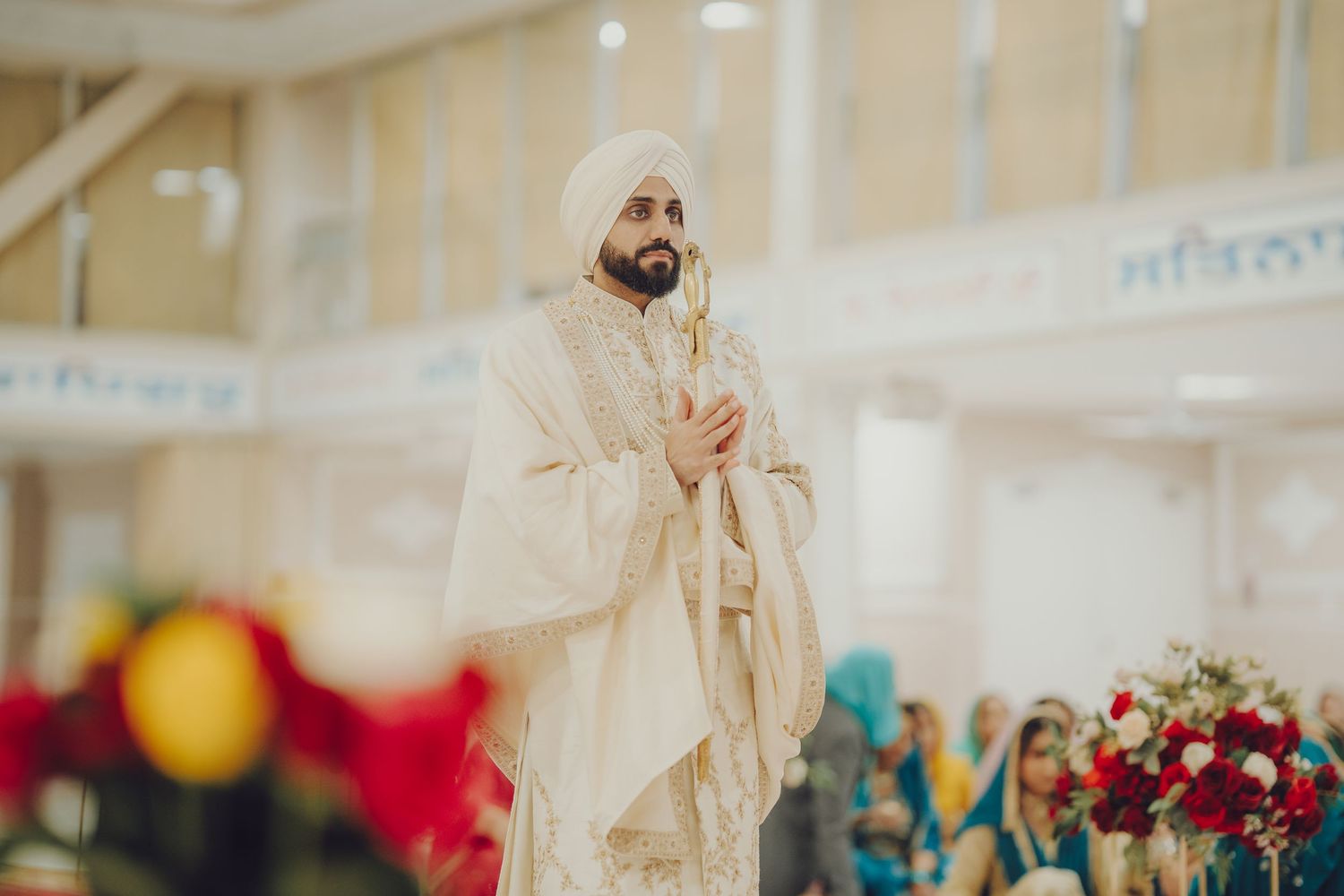Traditional Sikh ceremony participant in cream-colored attire standing in temple hall.