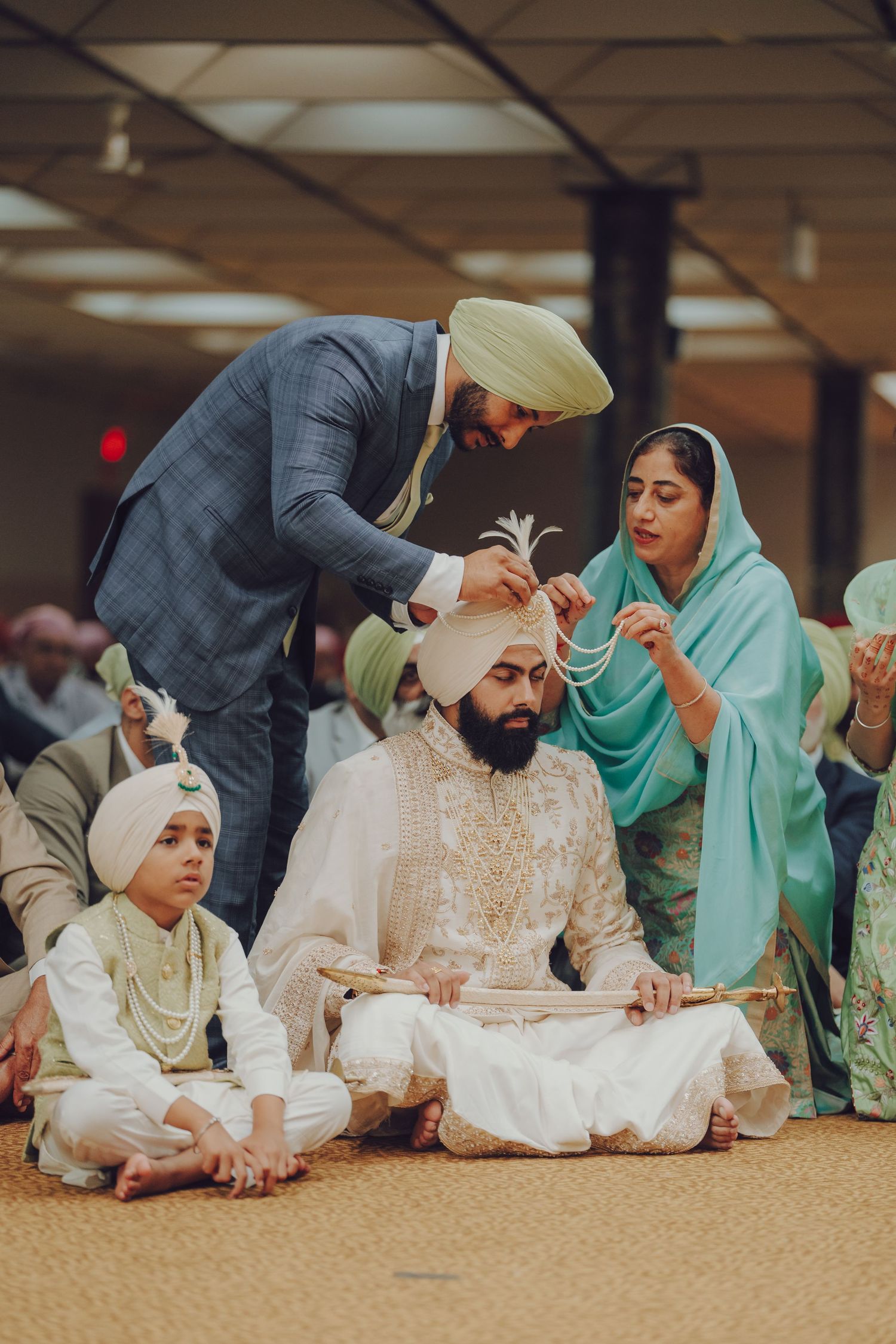 Sikh wedding ceremony showing couple sitting together during traditional rituals on carpeted floor.
