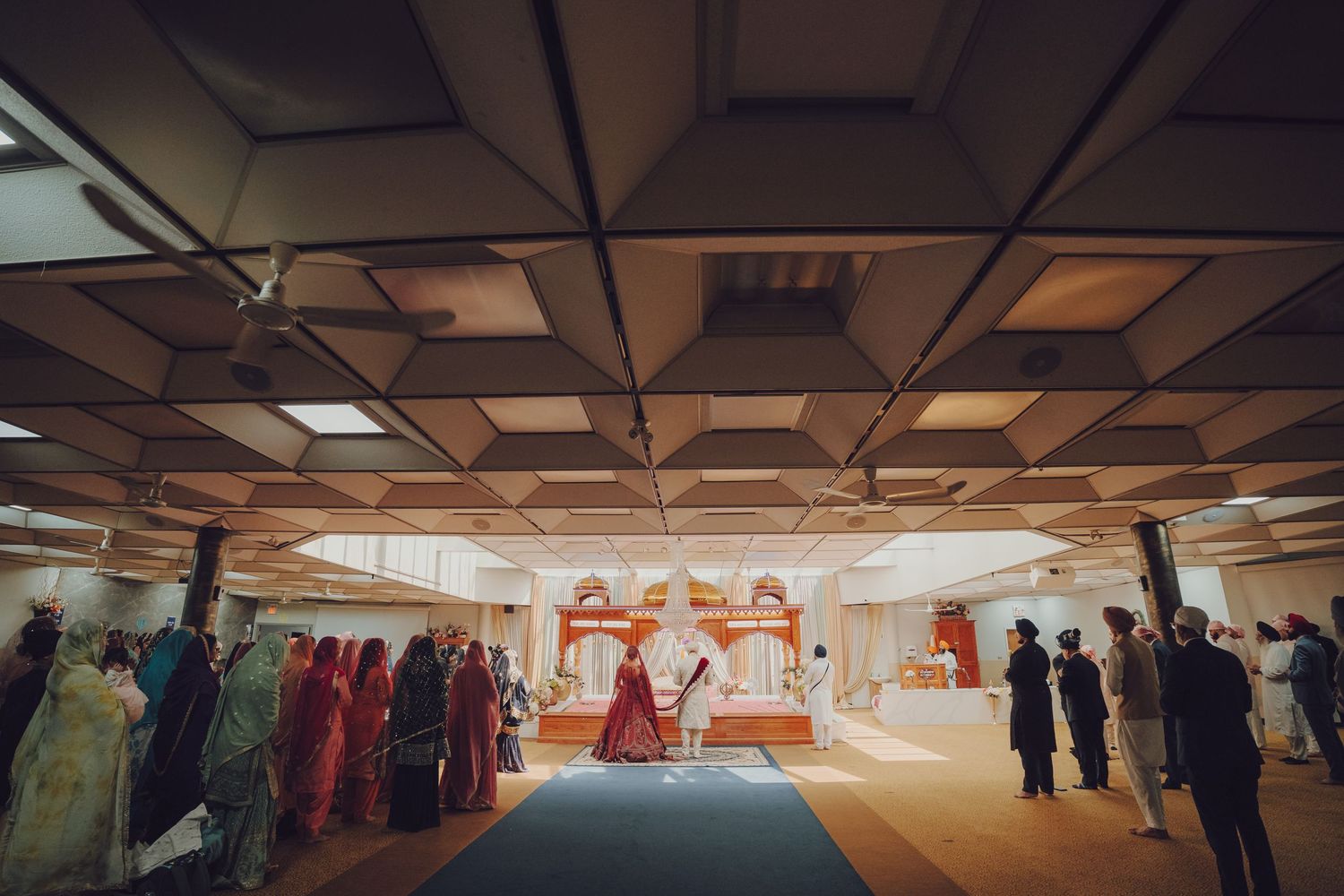 Wide shot of traditional Indian wedding ceremony venue with decorative ceiling and gathered guests.