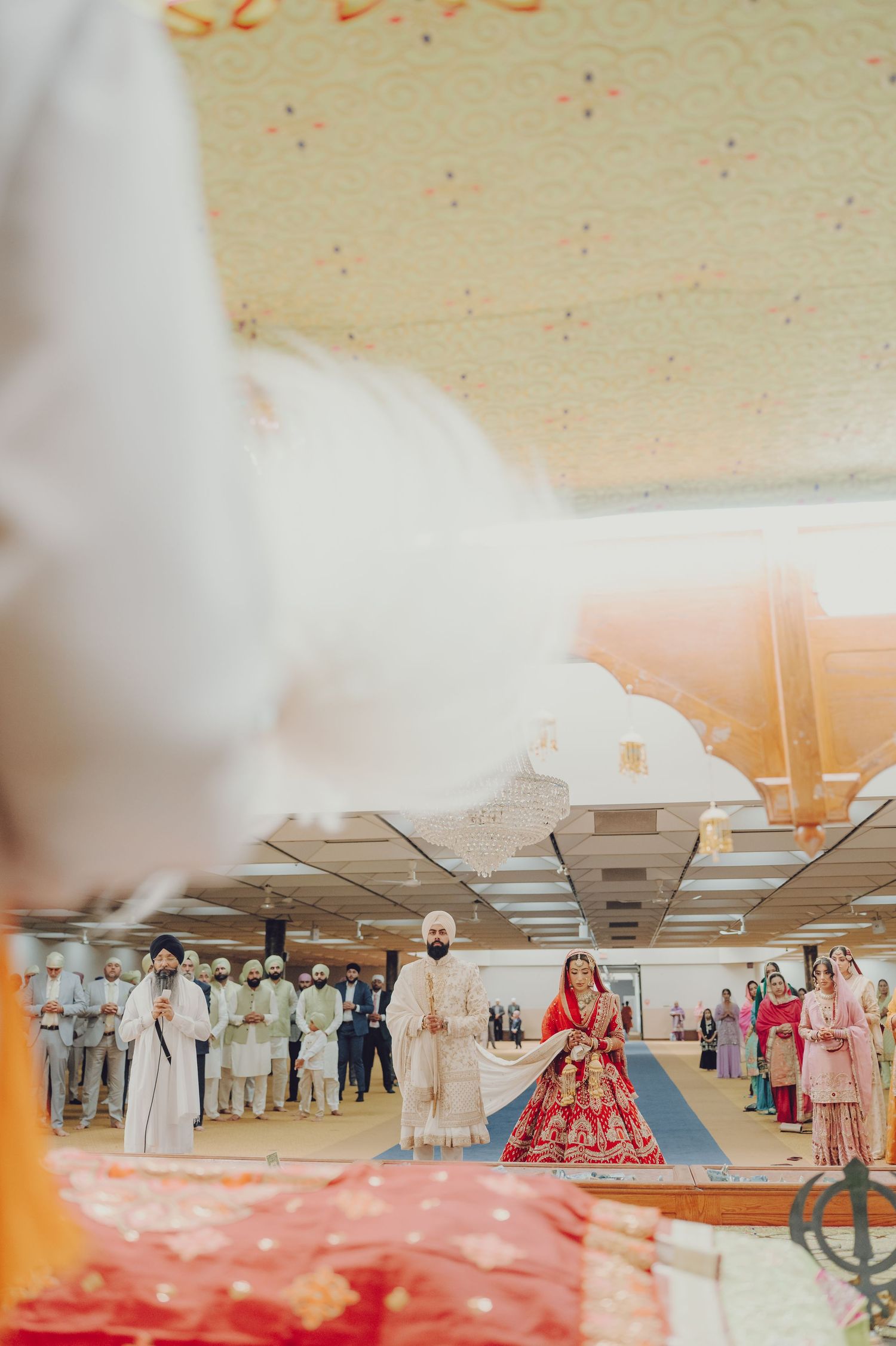 Aerial view of Sikh wedding ceremony with guests seated on floor in traditional gurdwara setting.