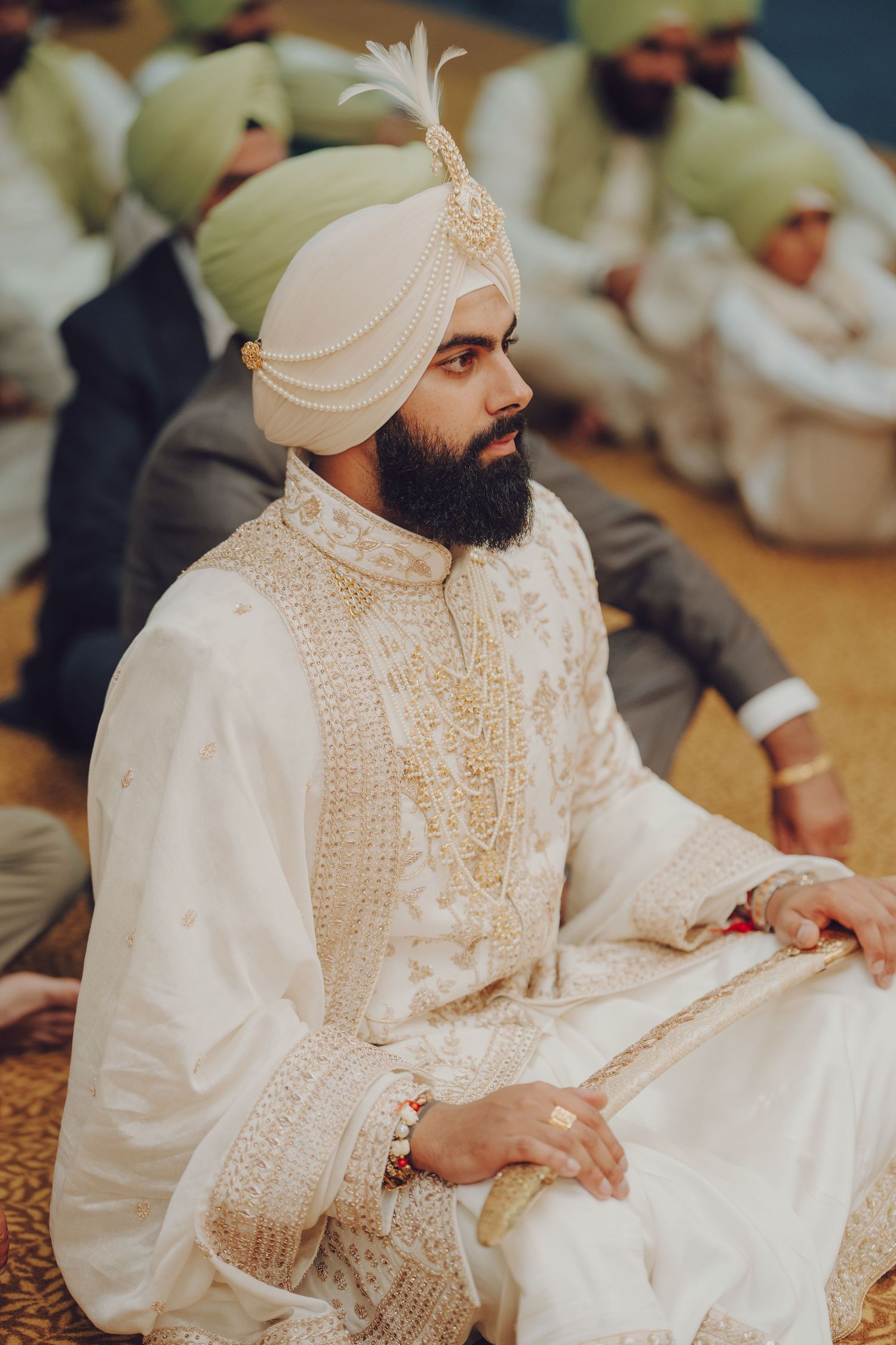 Groom in traditional Sikh wedding attire seated during religious ceremony.