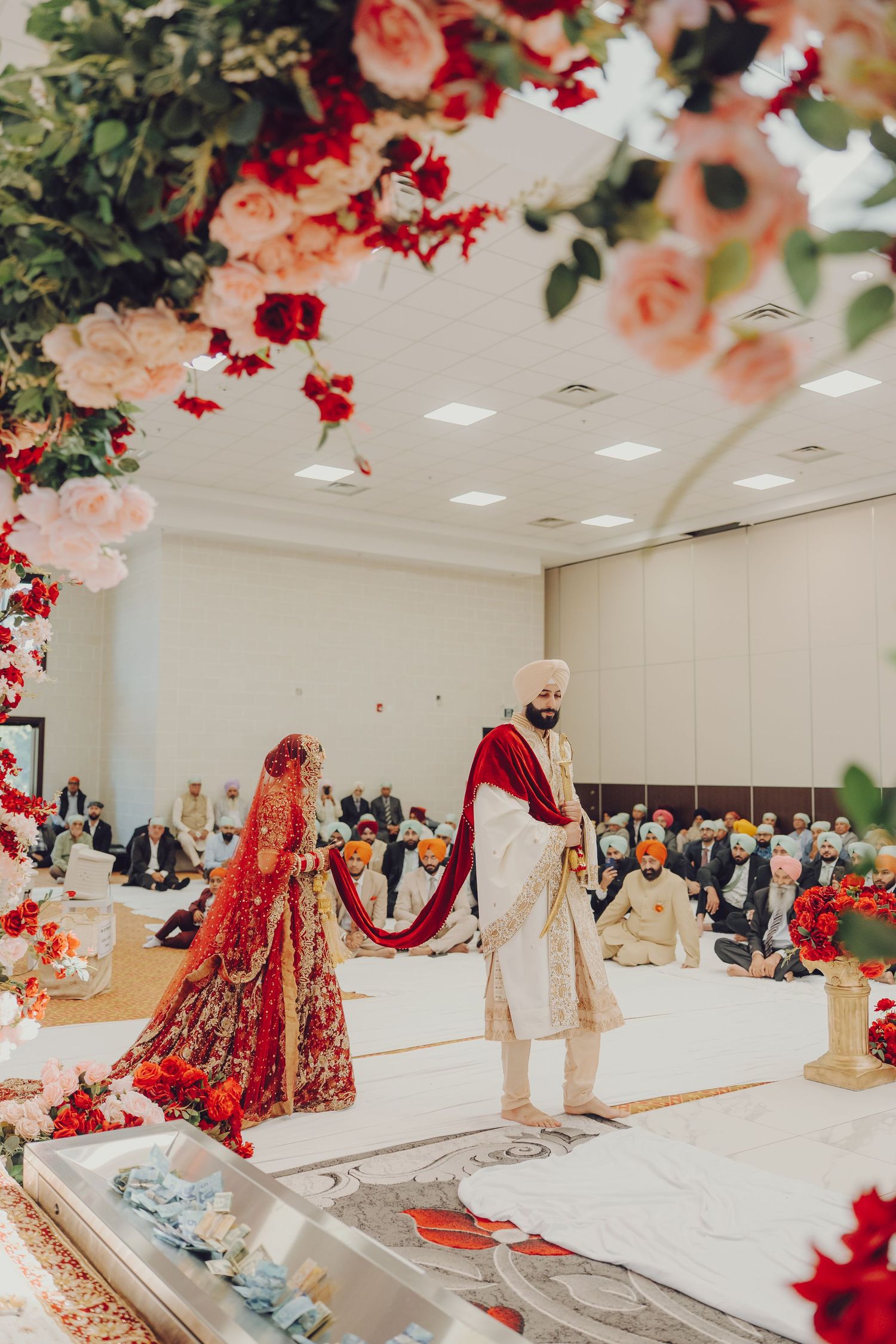 Sikh wedding ceremony setup with floral decorations and red drapery in a bright indoor venue.