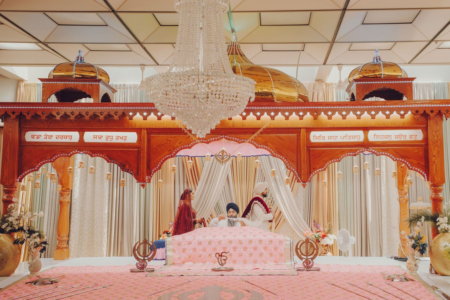 Elegant wedding venue setup with white drapes, chandeliers and traditional Indian decorative elements.