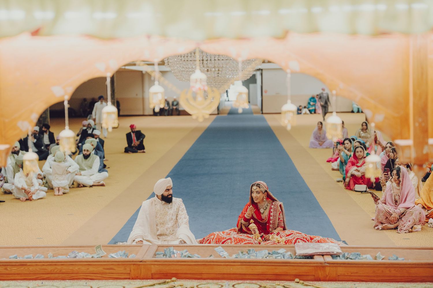 Panoramic view of a religious ceremony with attendees seated on floor mats in a large hall.
