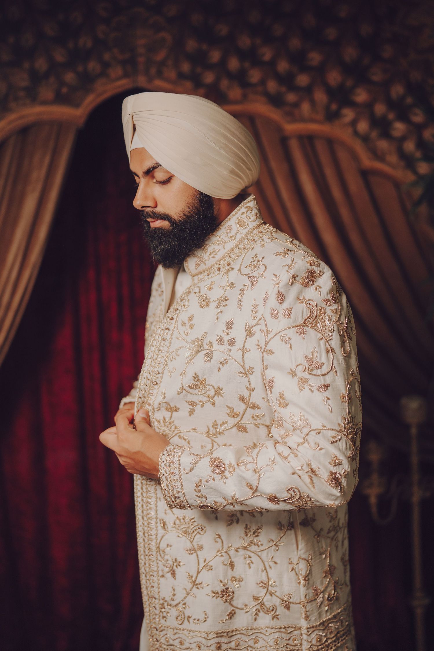 Traditional Sikh groom in ornate cream and gold sherwani outfit preparing for wedding ceremony.