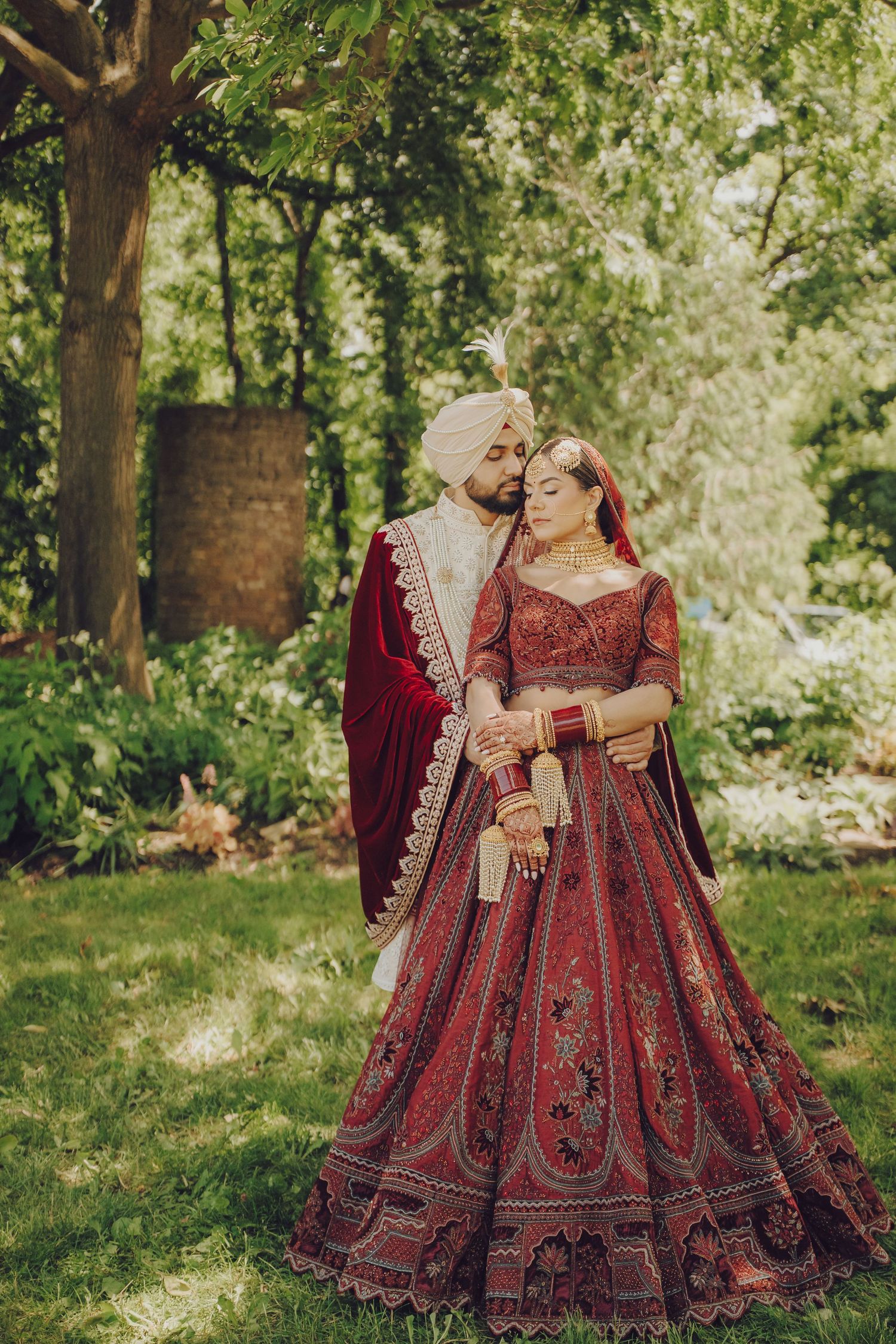 Ornate red and gold wedding lehengas displayed in a lush garden setting with natural sunlight.