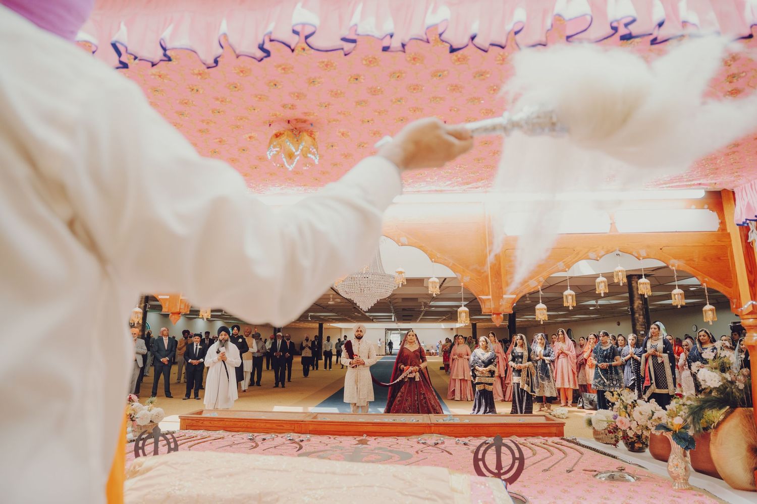 Panoramic shot of wedding guests gathered for a traditional Sikh ceremony in an indoor venue.