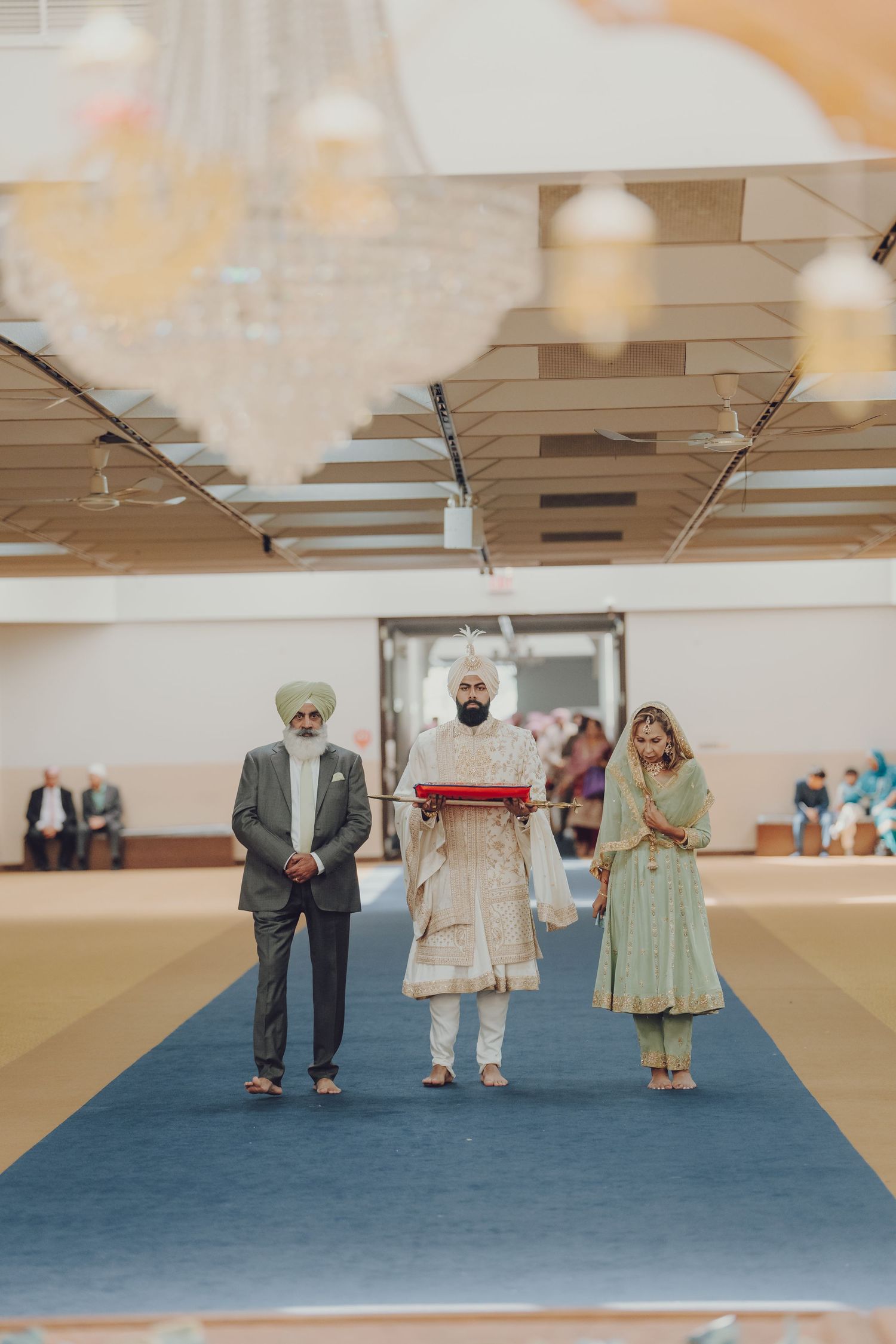 Wedding ceremony procession on blue carpet showing traditional Sikh attire.