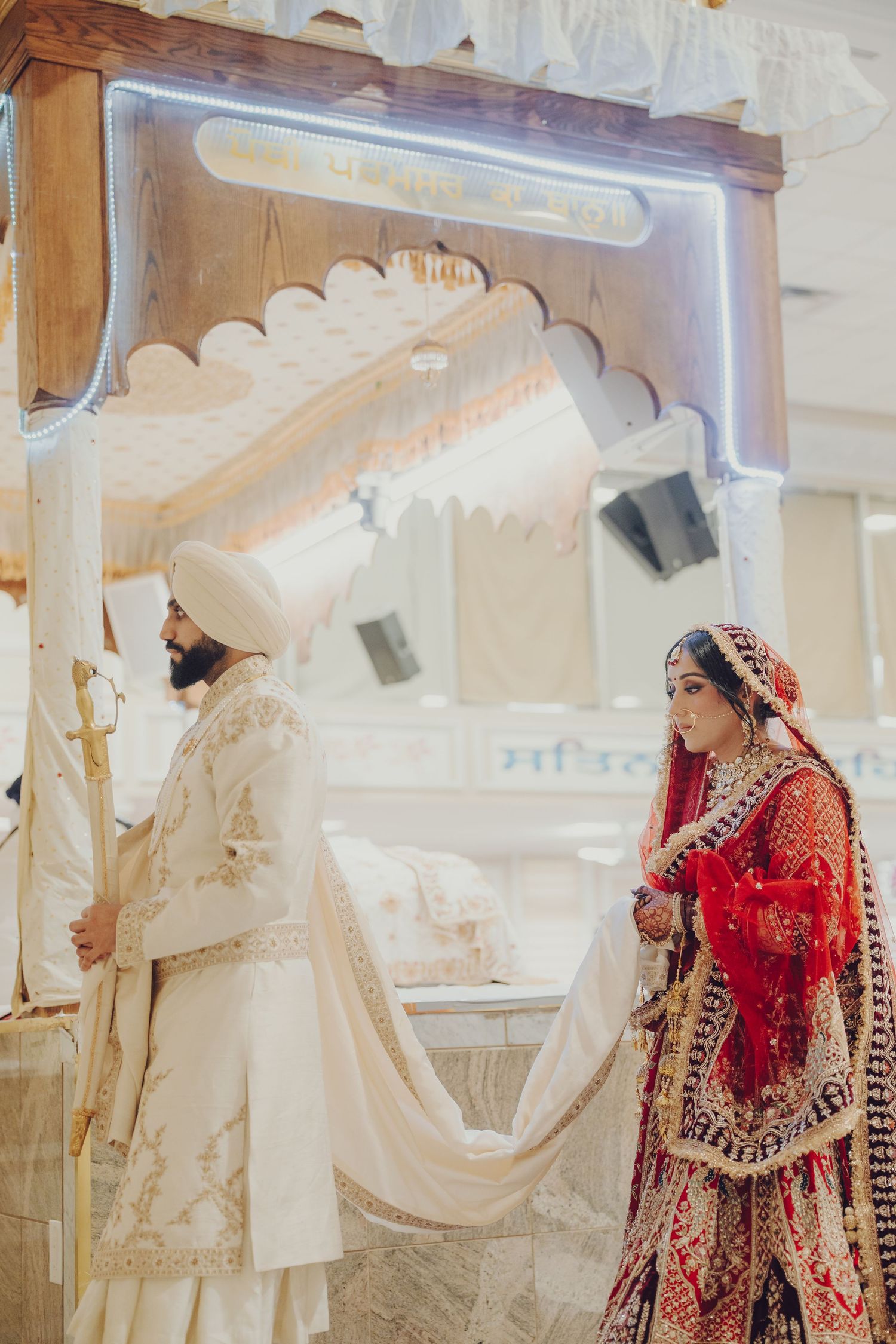 A traditional Sikh wedding ceremony with the couple in ornate white and red traditional attire under an archway.