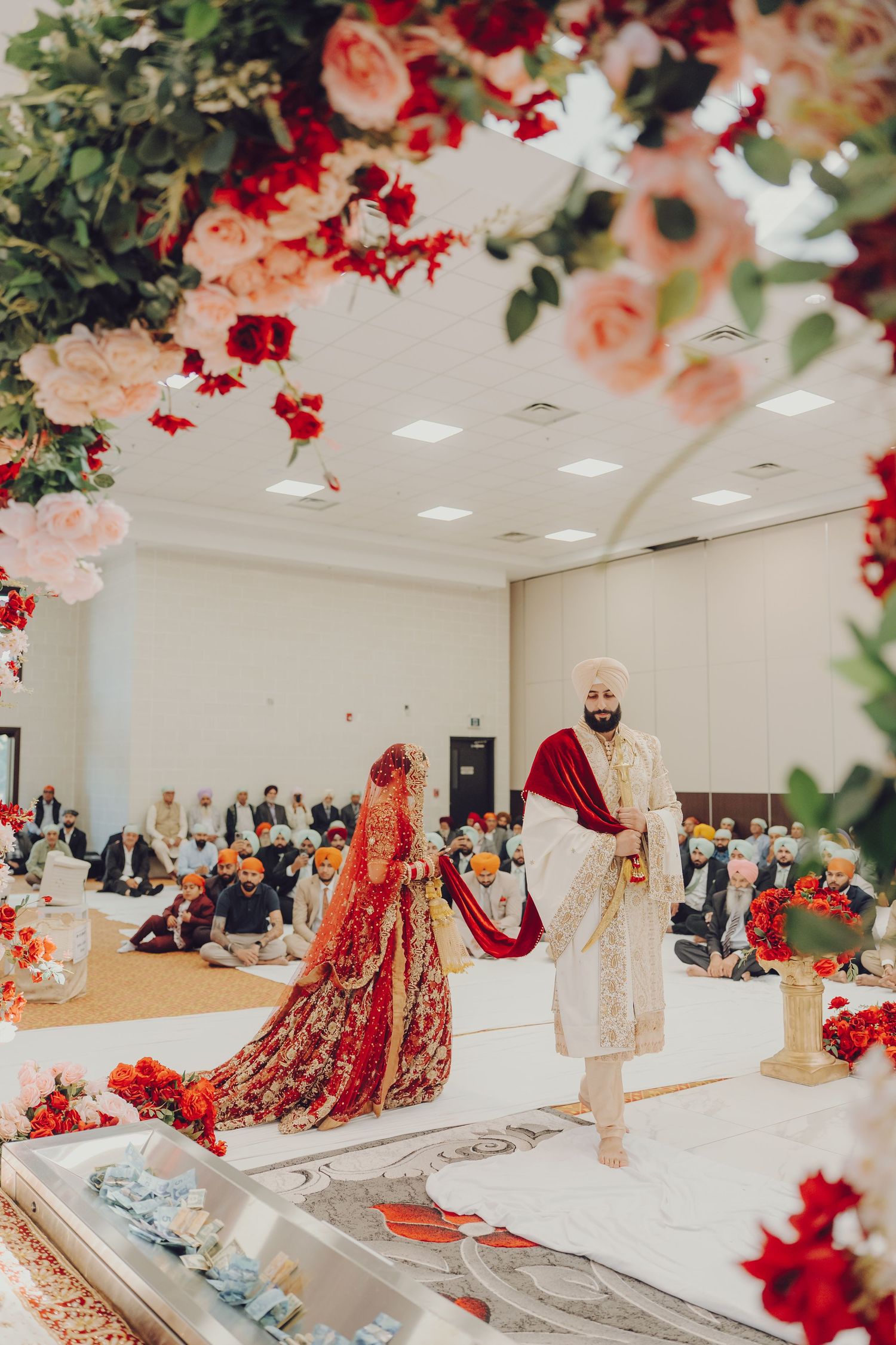 Traditional Indian wedding ceremony setup with red and peach floral decorations adorning a white mandap stage.
