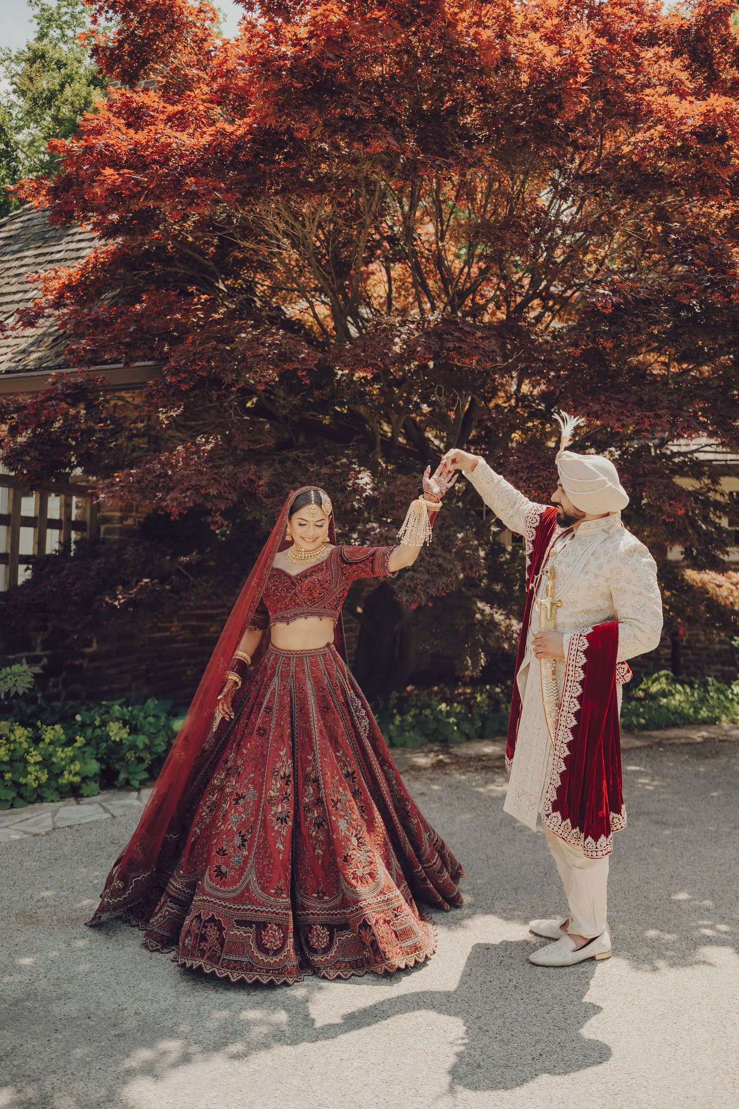 Autumn wedding photoshoot with couple in traditional Indian attire against red maple trees.