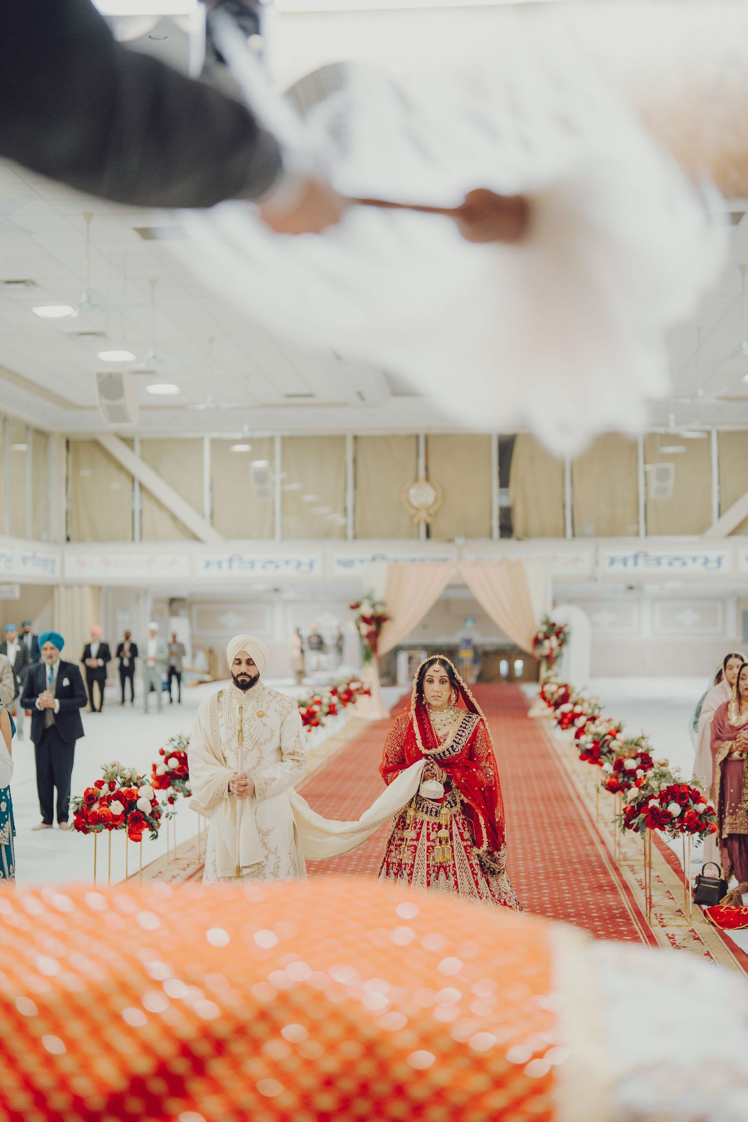 Wide shot of a Sikh wedding ceremony aisle with red carpet and floral decorations.