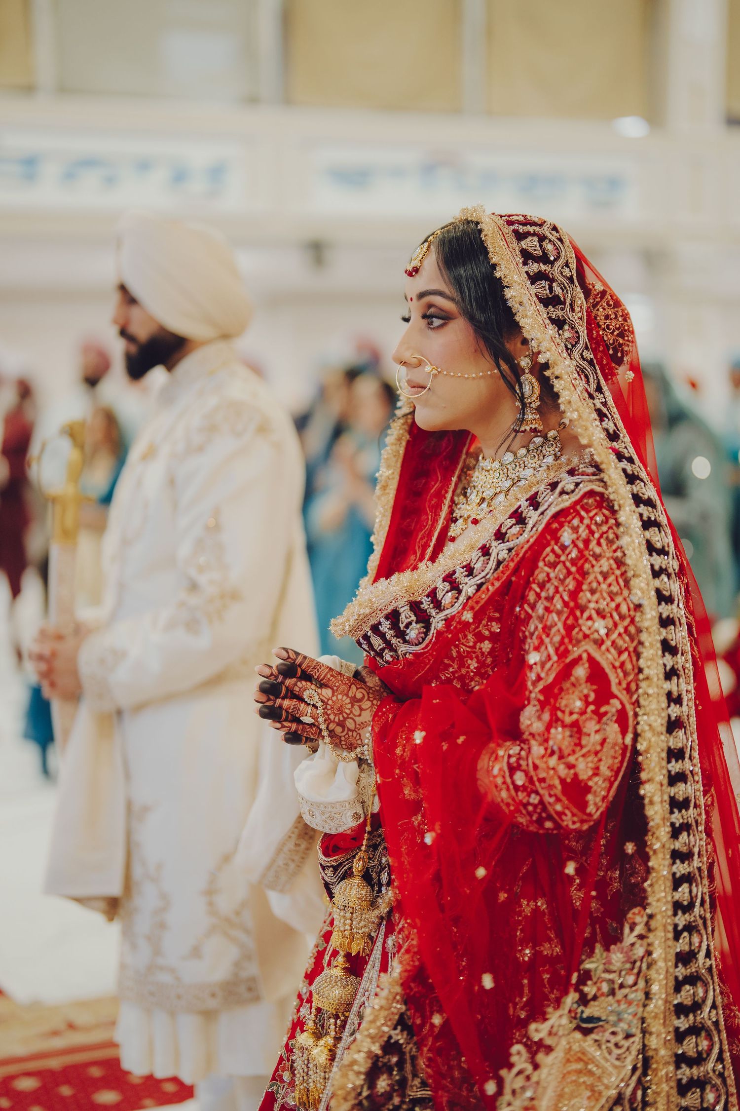 A bride in a traditional red and gold South Asian wedding lehenga performs religious rituals during a ceremony.