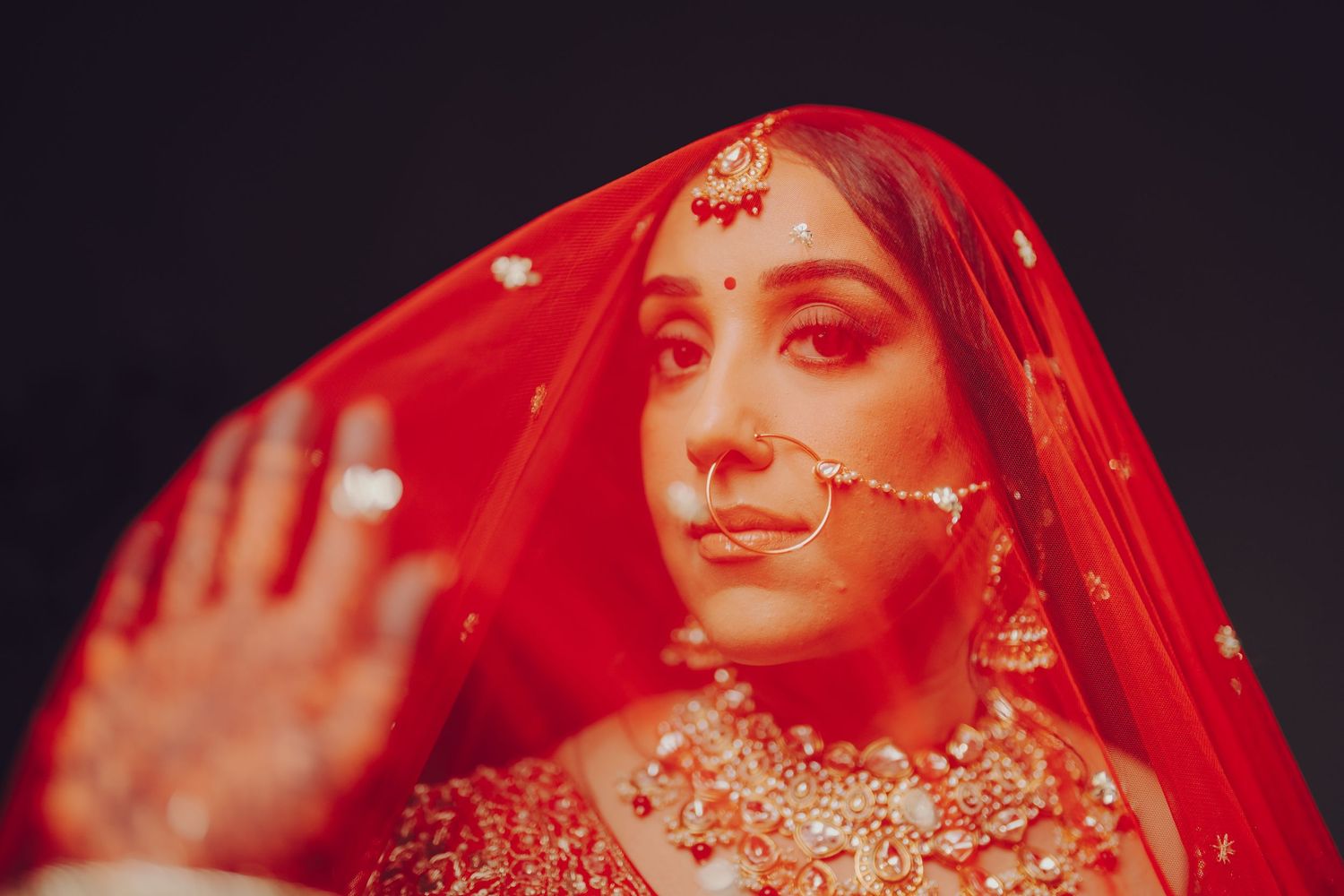 A bride in traditional red wedding attire poses with a veil during a South Asian wedding ceremony.