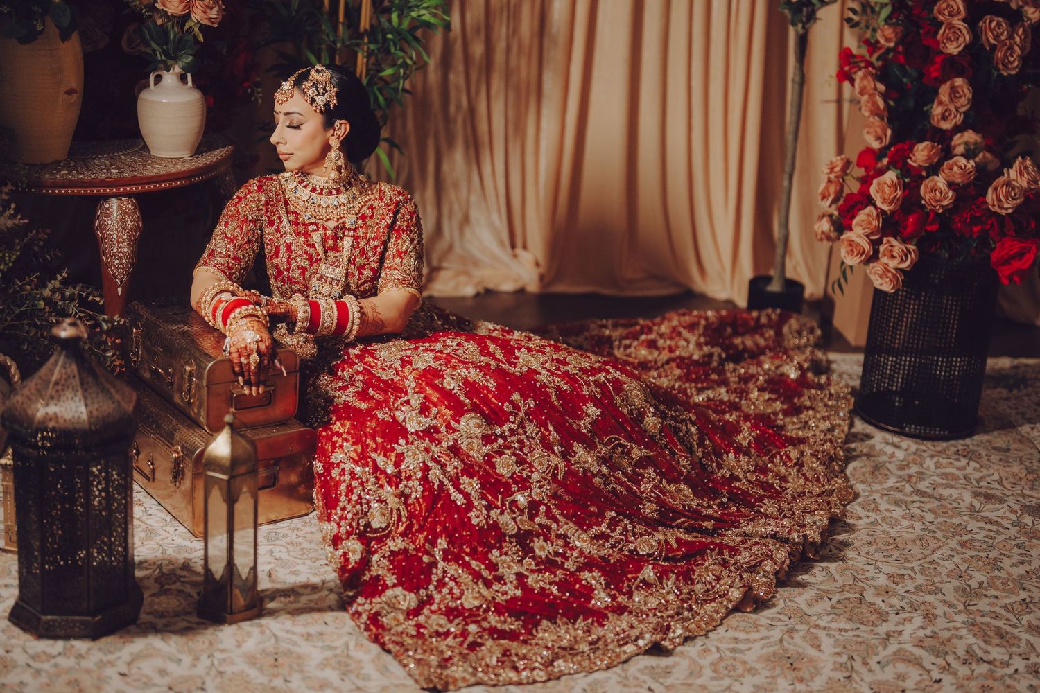 Ornate red and gold embroidered bridal lehenga displayed in multiple angles against elegant curtained backdrop.
