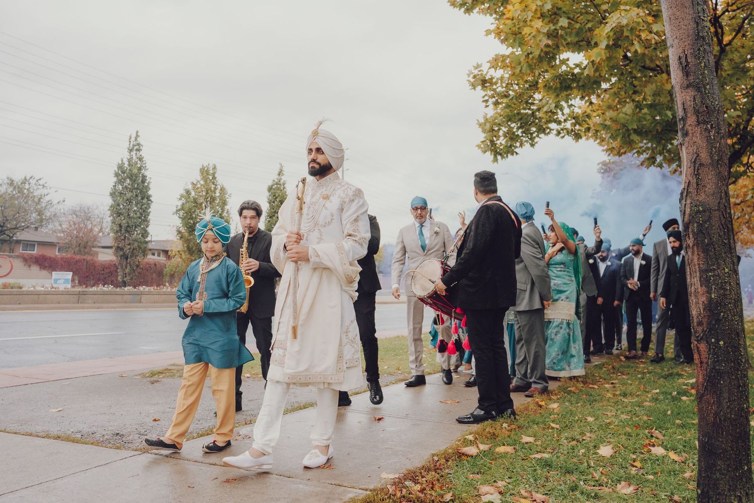 Wedding party members in teal and white attire pose for photos along a scenic waterfront during autumn.
