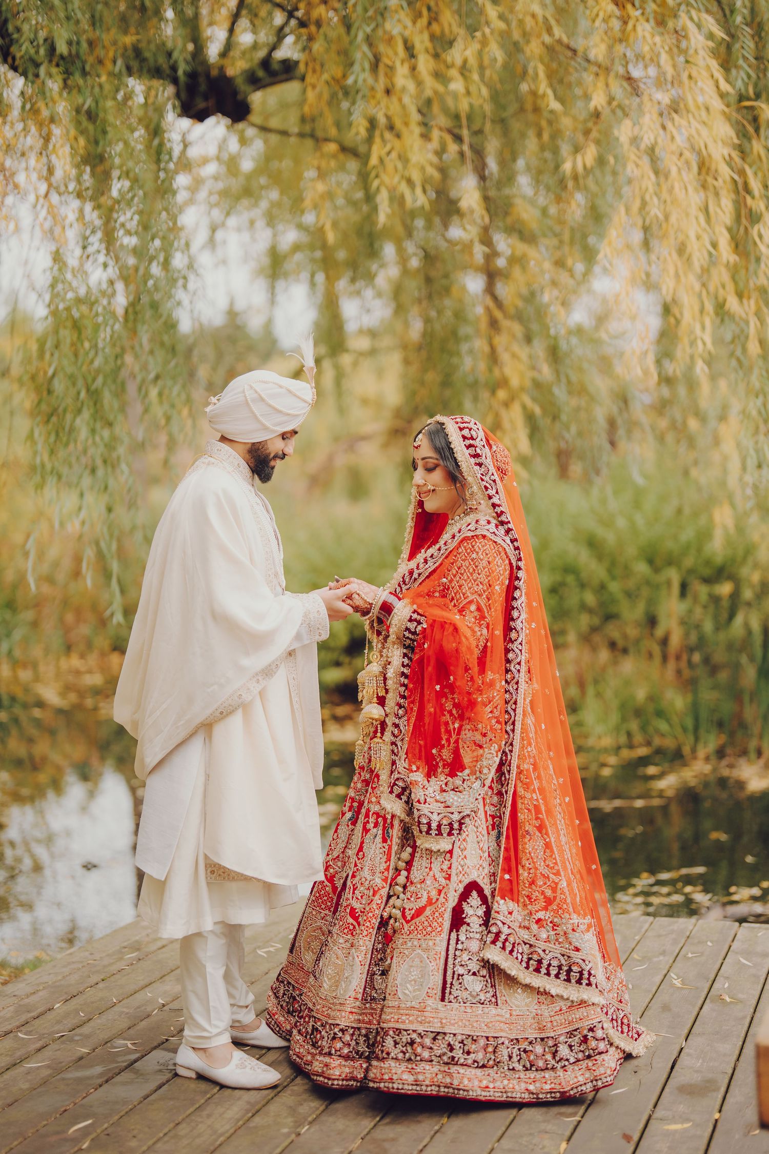 Romantic wedding photoshoot on wooden deck with willow trees and pond in background.